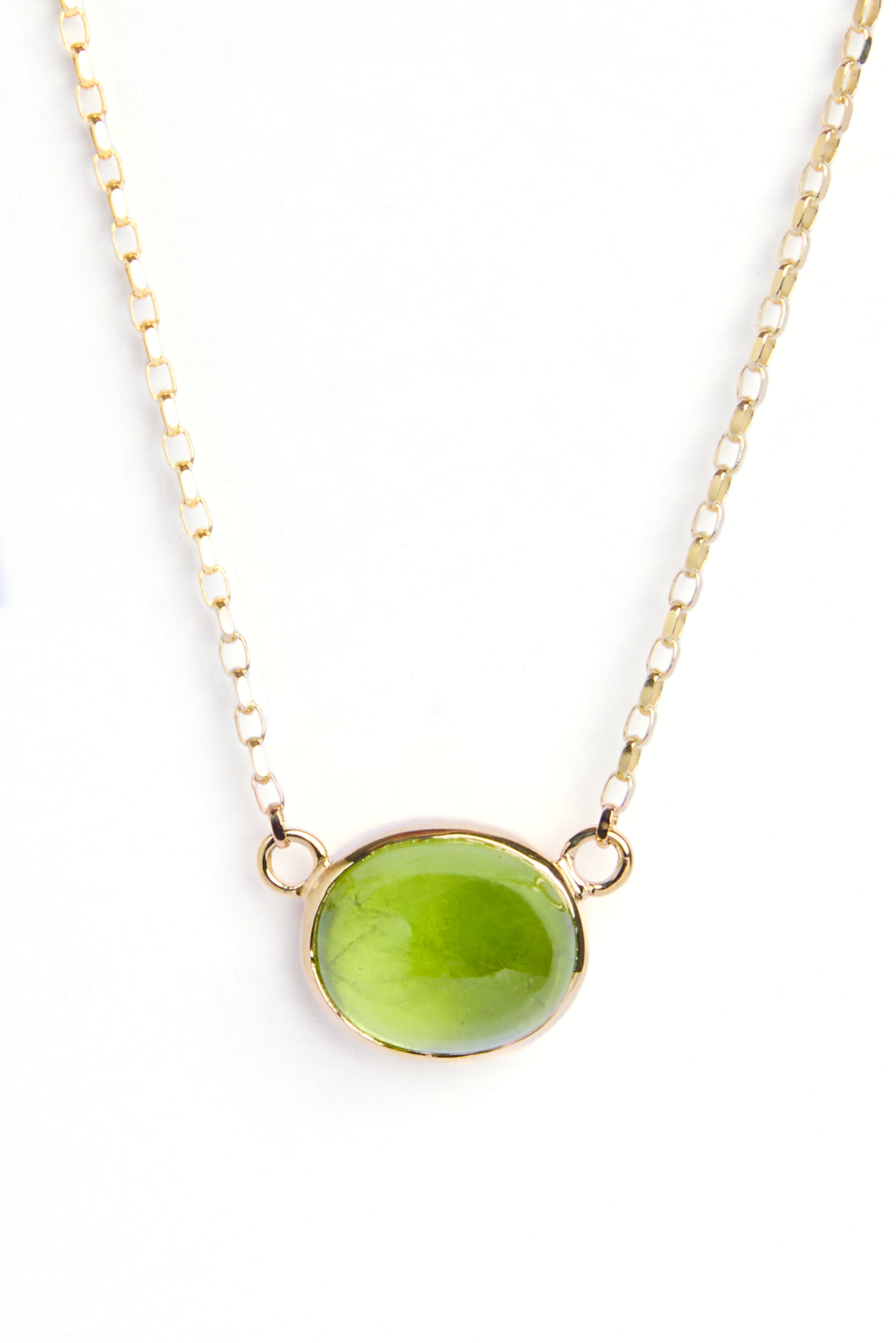 The Whispering Moss 9ct Yellow Gold Necklace by Madeleine Fine Jewellery features an oval green peridot gemstone in a simple gold bezel, shown on a white background.