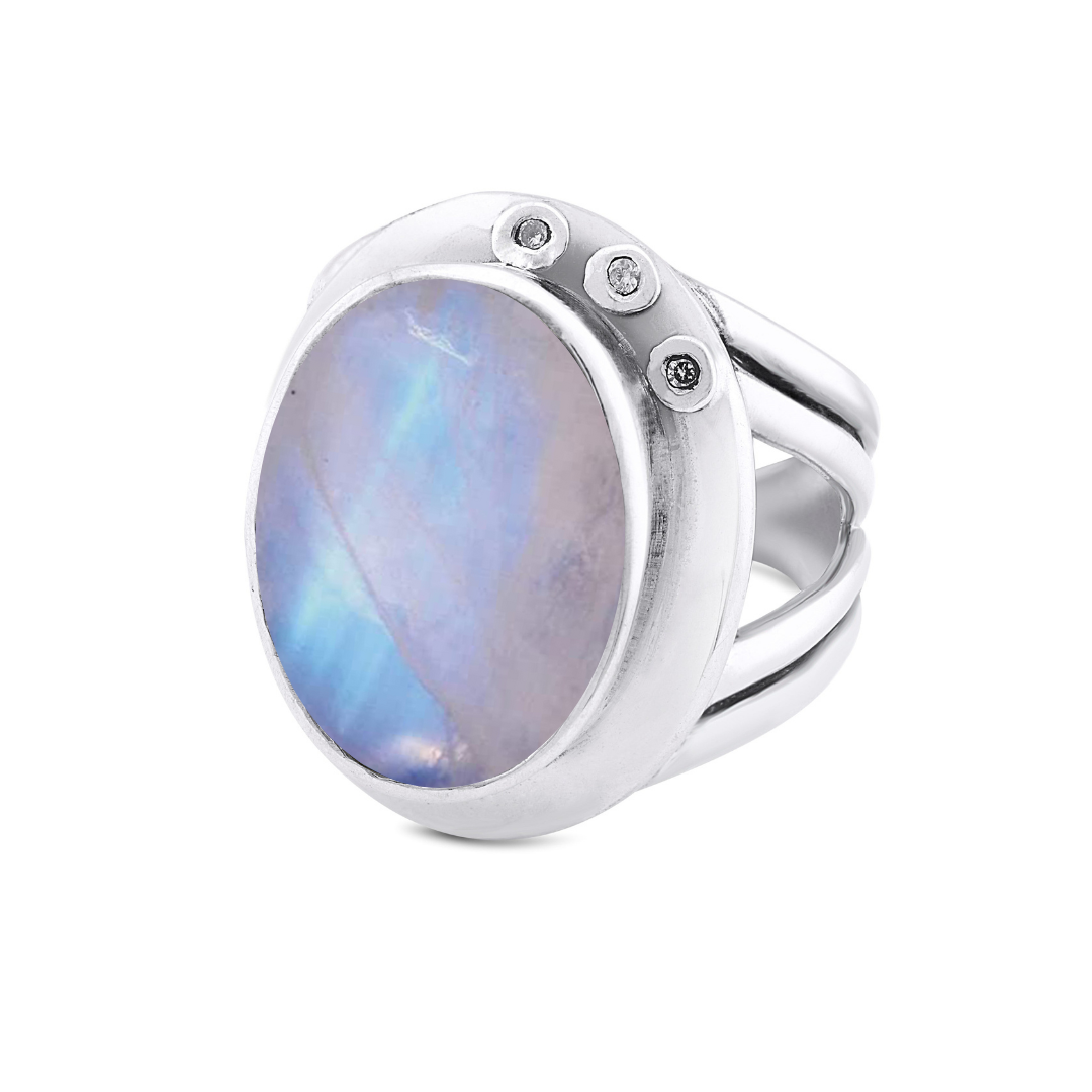 Gallardo & Blaine Designs' Eyetelia Ring features a large oval iridescent gemstone in blue-purple hues, accented by three clear stones. This eye-catching, adjustable sterling silver statement ring suits any occasion.