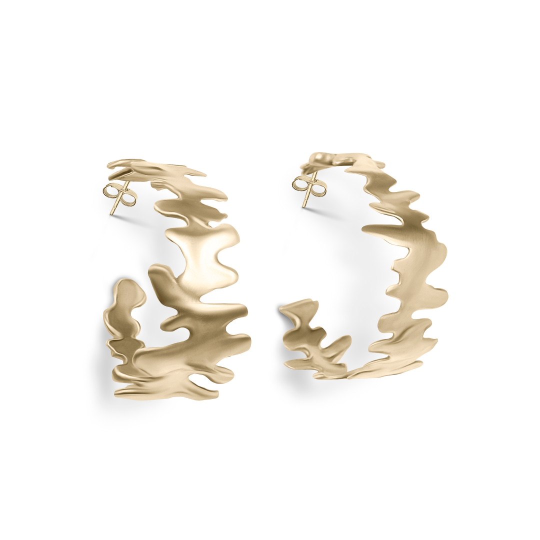 The Lava Hoops by Madeleine Blaine are gold earrings featuring an abstract, wavy design reminiscent of sculptural jewelry, displayed against a plain white background.
