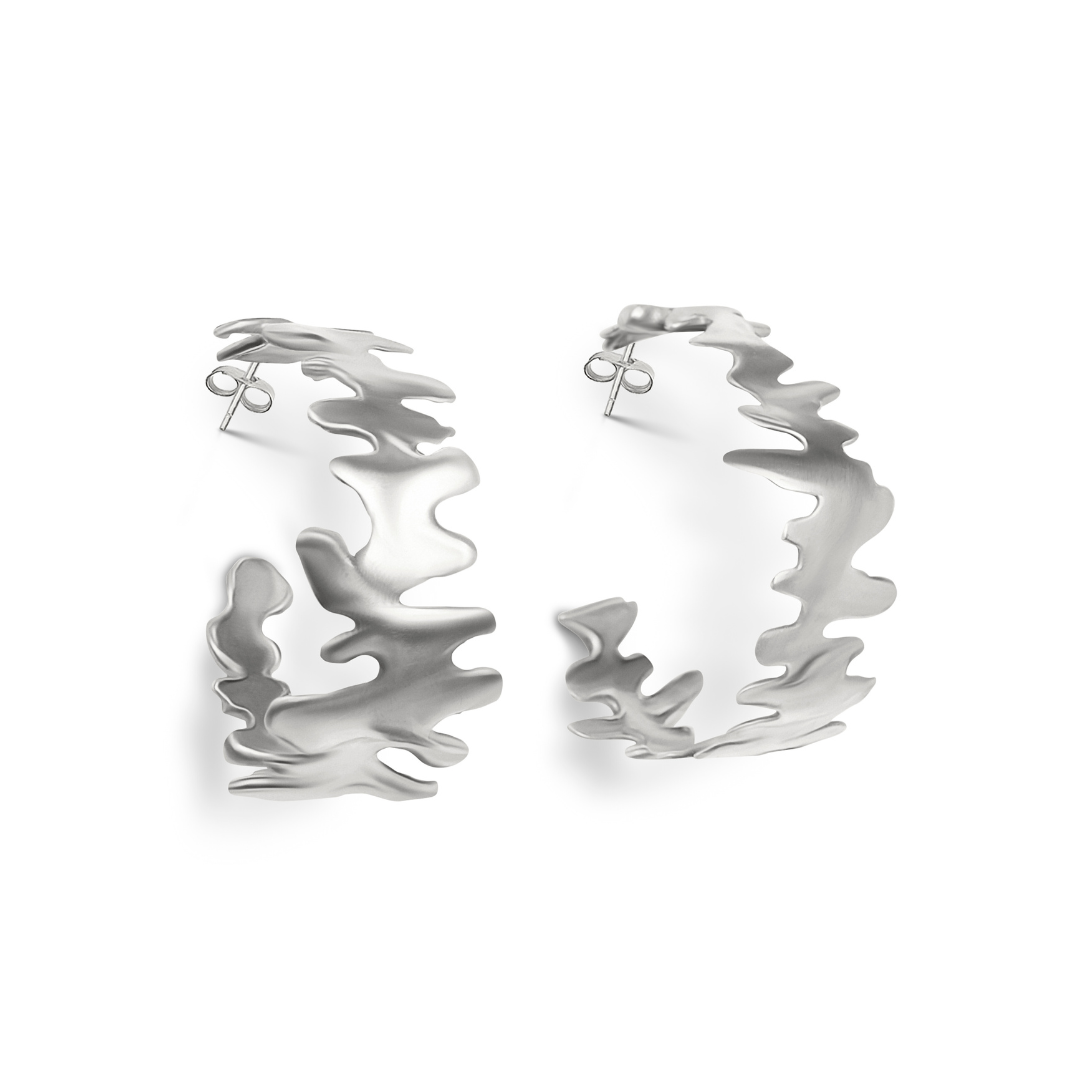 Madeleine Blaine’s Lava Hoops feature abstract, wavy, organically cut-out edges that showcase sculptural artistry. These hand-carved silver earrings have a matte finish, secure post back closures, and are elegantly displayed on a white background.
