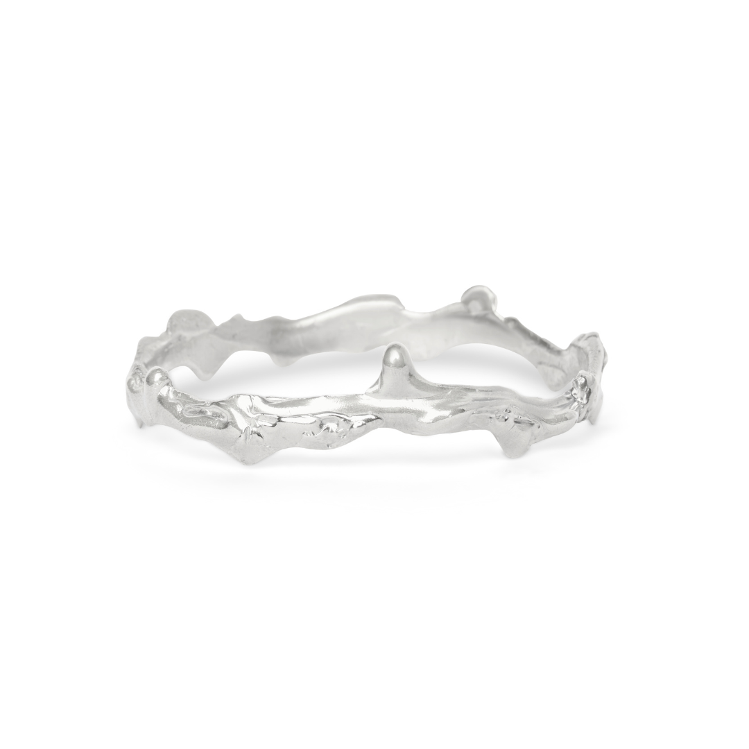 Introducing the Liana Bangle by Madeleine Blaine: a silver bangle featuring an organic, textured, and uneven design reminiscent of twigs or branches. Photographed on a white background, it perfectly captures the artisanal charm characteristic of Dublin je