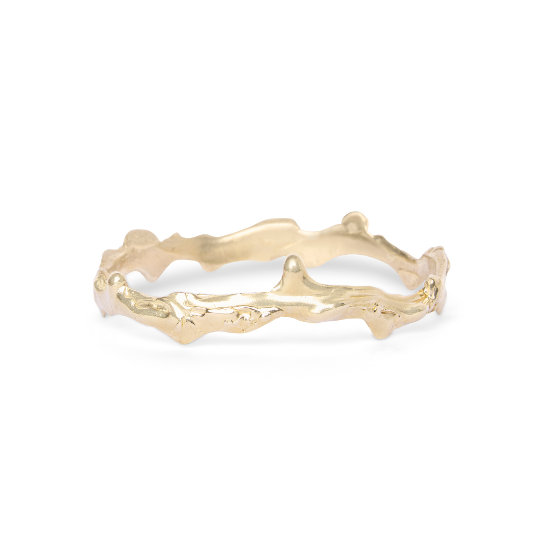 Madeleine Blaine’s Liana Bangle features an uneven, organic, textured gold band reminiscent of natural twigs or branches and is shown against a white background—this unique piece pairs beautifully with classic hoop earrings from Dublin jewelry collections