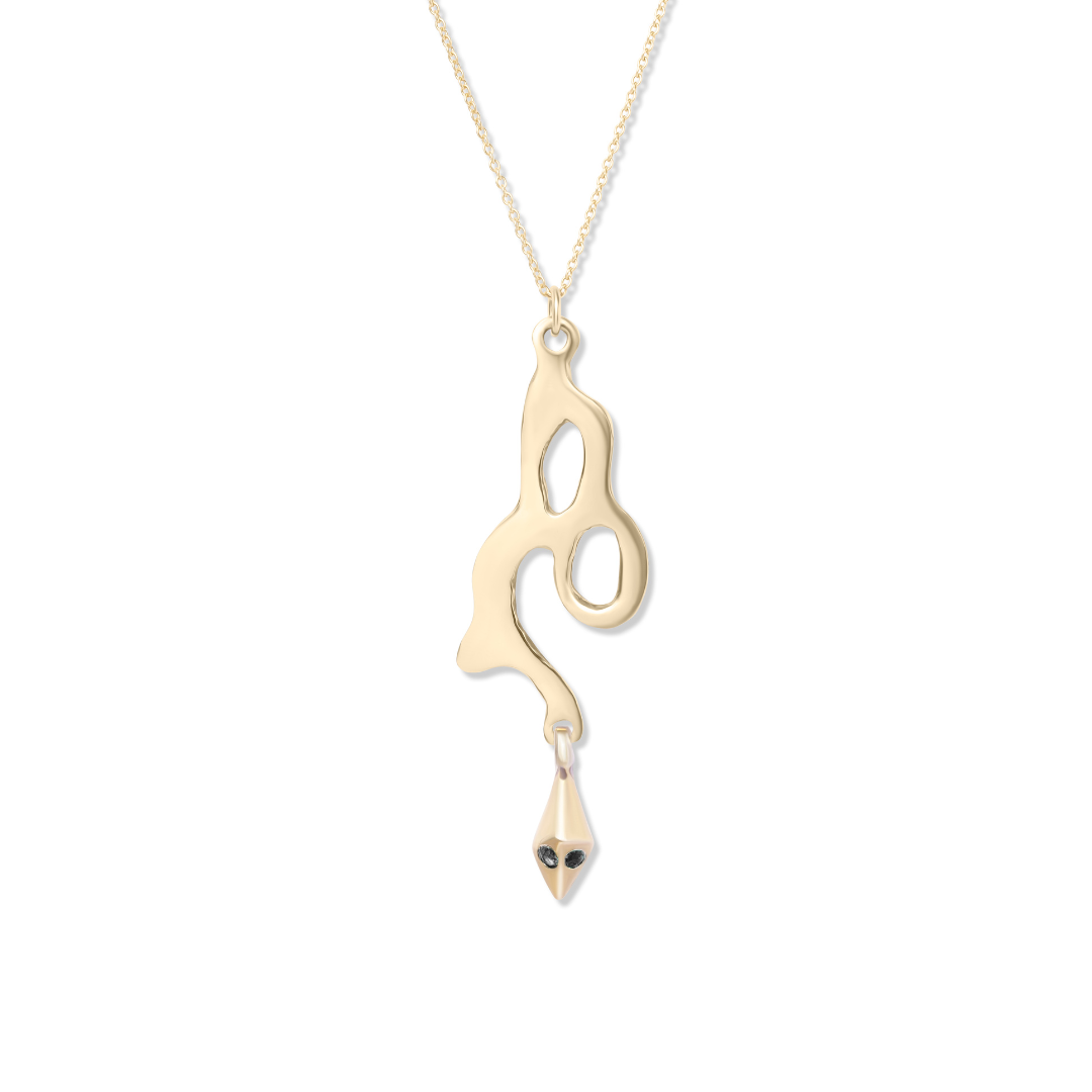 The Serpent Pendant by Madeleine Blaine showcases a hand-carved gold pendant with abstract flowing lines and open spaces, finished with a small geometric charm reminiscent of a squid’s form and accented by black eyes. Inspired by the intricate artistry of