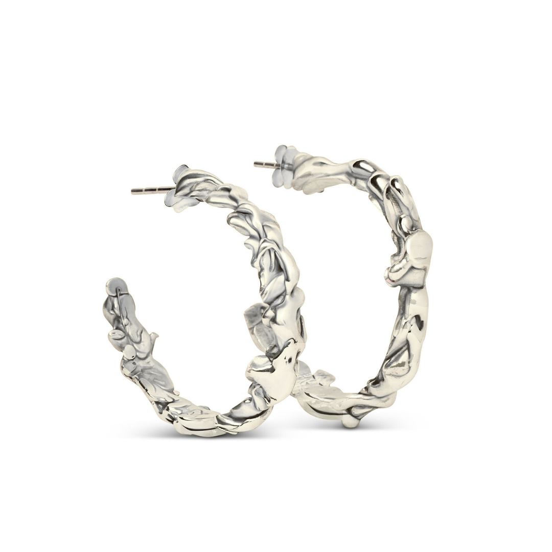 The Molten Hoops Small by Madeleine Sculptural Jewellery—silver earrings with a textured, wavy design—stand upright against a white background, showcasing the artistry of hand-carved jewellery.