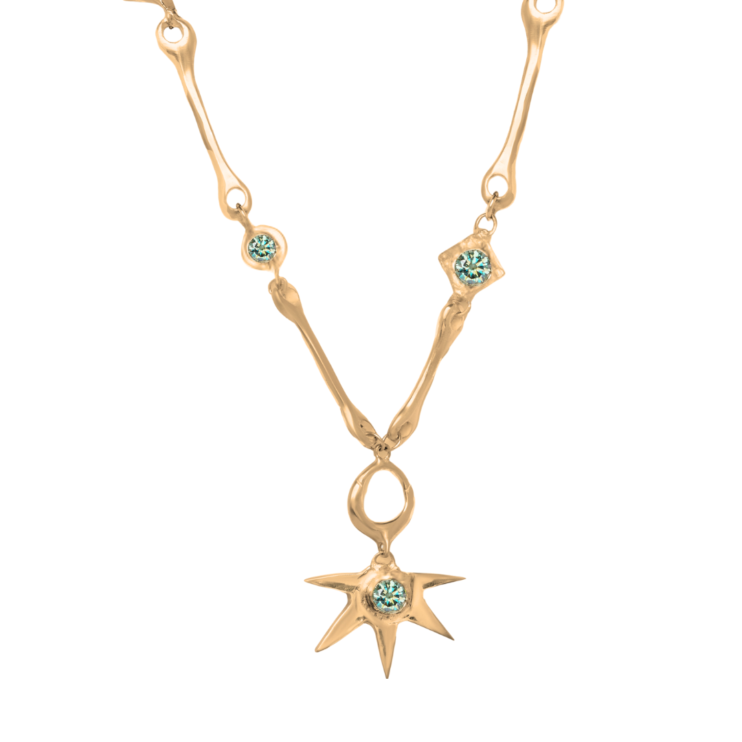 Discover the Réalta Necklace with Moissanite by Madeleine Blaine, featuring an organic, branch-inspired gold chain adorned with light blue gemstones. The pendant showcases a spiked star design centered with a luminous blue Moissanite gem, elegantly suspen