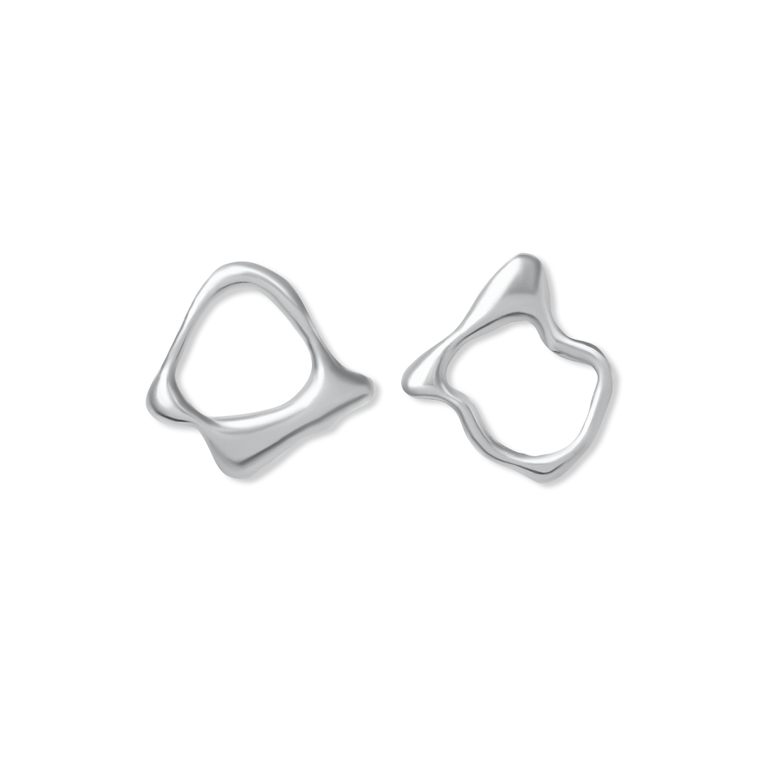 Two abstract, asymmetrical silver earrings with wavy, organic shapes set against a white background. Reminiscent of hand-carved jewelry, the Asymmetrical Molten Studs by Madeleine Blaine feature smooth, polished finishes and distinctive, irregular outline
