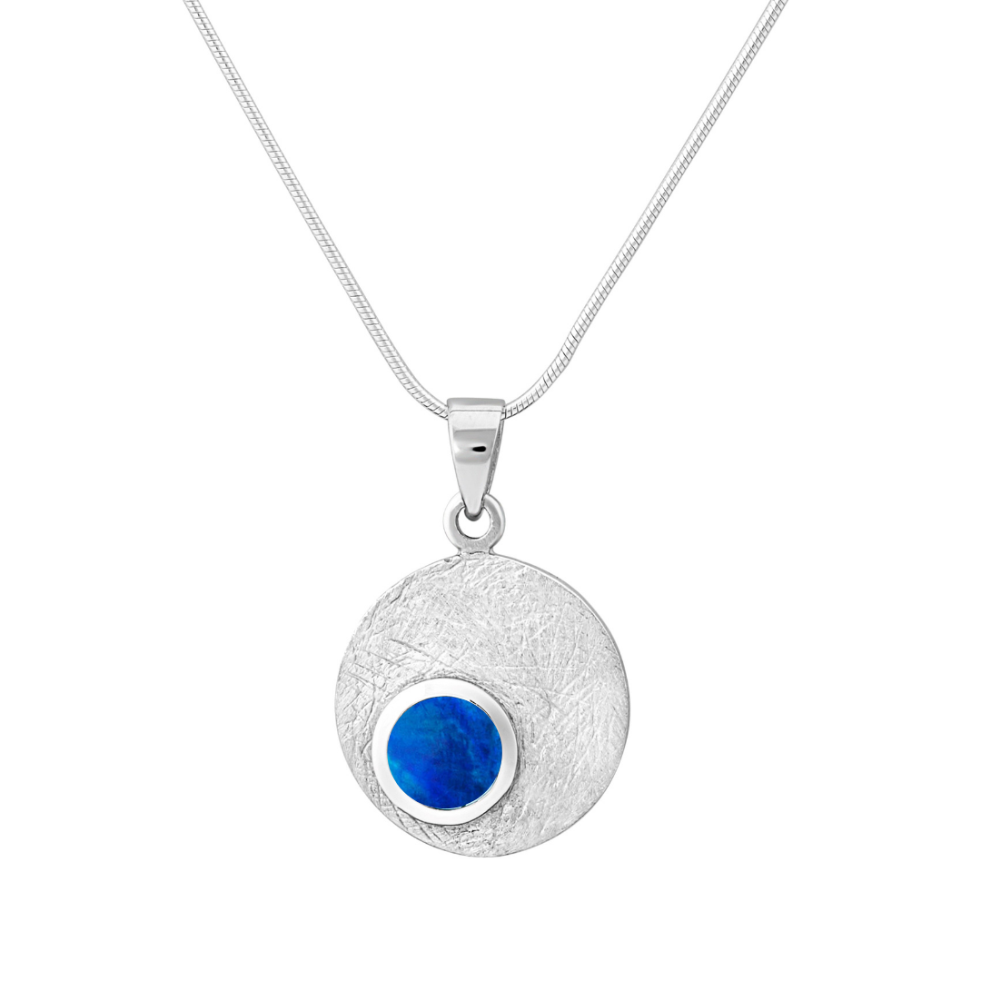 The Selene Necklace Silver - Small by Gallardo & Blaine Designs features a round, textured sterling silver pendant with an off-center gemstone, beautifully displayed on a thin silver chain.