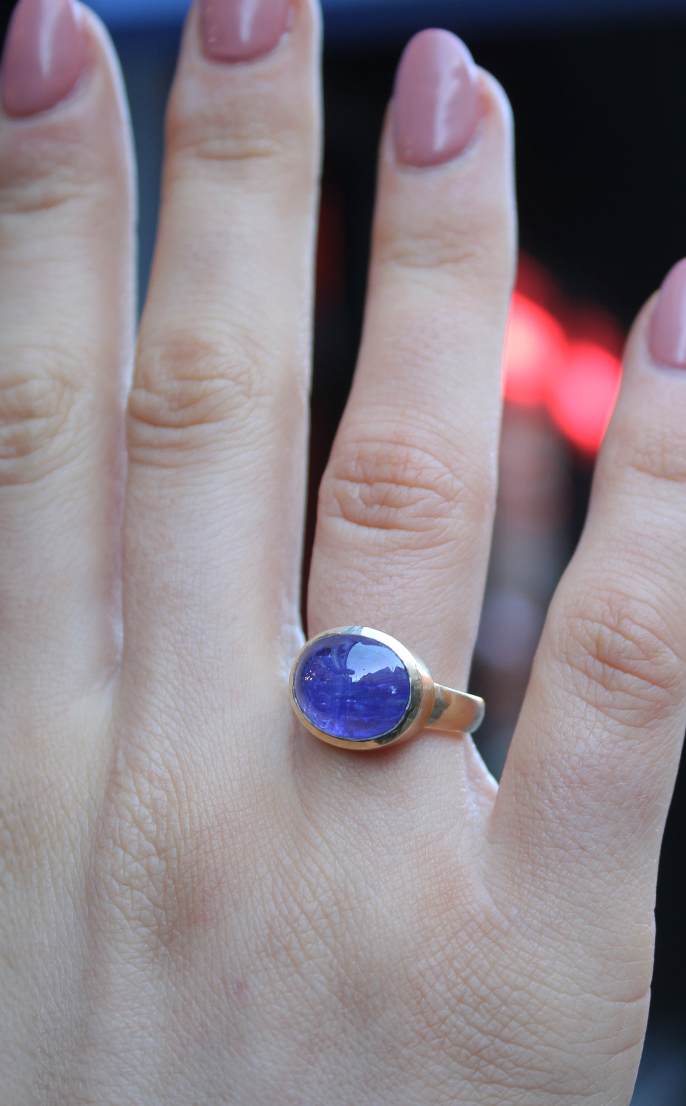 9ct Yellow gold ring with a large oval cabochon Tanzanite, which is a dark blue purple colour. The 9ct yellow gold band is D shaped with the widest at the back at 3mm. Shown here on a ring finger
