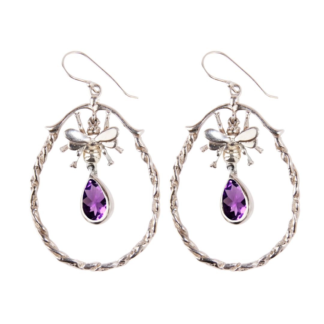Watermelon Tropical’s Wildlife Large Bee Hoop Drops feature a silver hoop with a bee at the top and a teardrop-shaped purple gemstone inside a twisted oval frame—whimsical earrings for adding charm to your style.