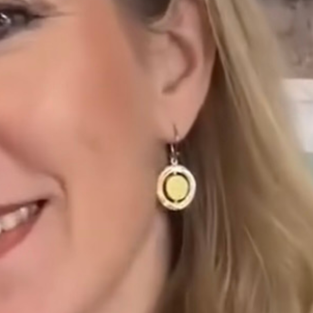 Close-up of a smiling woman with blonde hair, showcasing her ear adorned with Gallardo & Blaine Designs’ Urú Dangle Earring—round sterling silver with a yellow center and silver border.