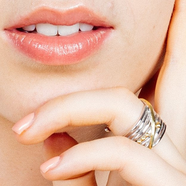 Close-up of a person’s lower face and hand. Their lips are slightly parted, showing teeth. They wear the Bamboo Ring in Sterling Silver & Gold Vermeil by Gallardo & Blaine Designs on their middle finger, featuring intertwined sterling silver and gold verm