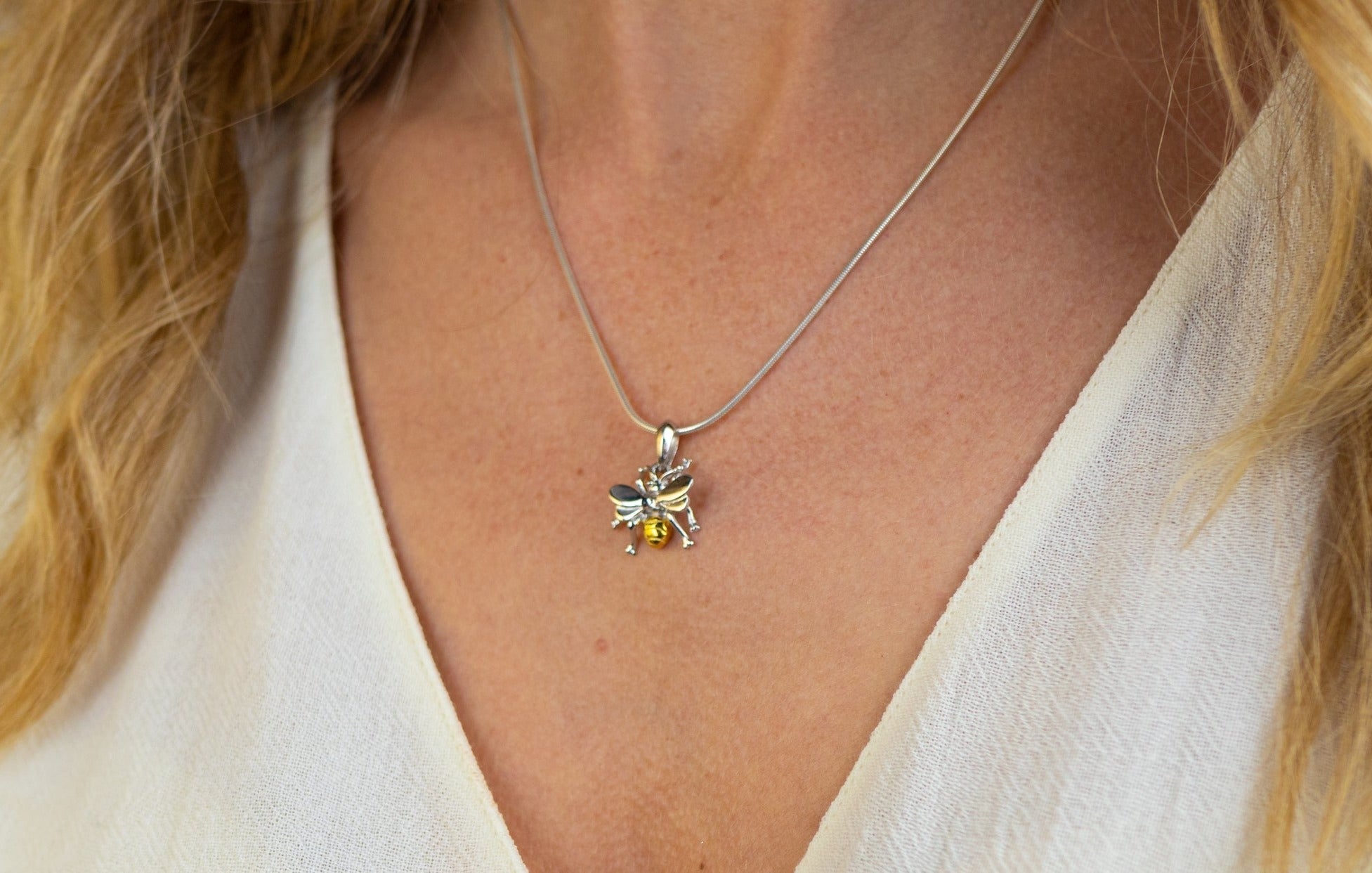 A close-up of a woman wearing the Watermelon Tropical Wildlife Pendant - Small Bee With Chain, featuring exquisite silver craftsmanship and gold-detailed wings, set against a cream-colored blouse.