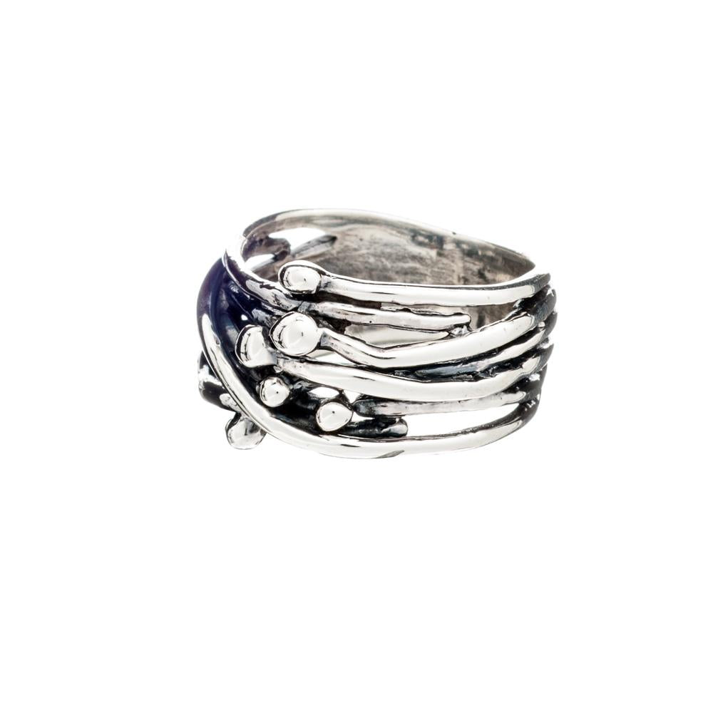 The Berry Ring in Silver by Gallardo & Blaine Designs features a unique, intertwined band design with multiple strands, some adorned with small, round silver beads. The ring has a modern, artistic aesthetic with a textured and polished finish, making it a