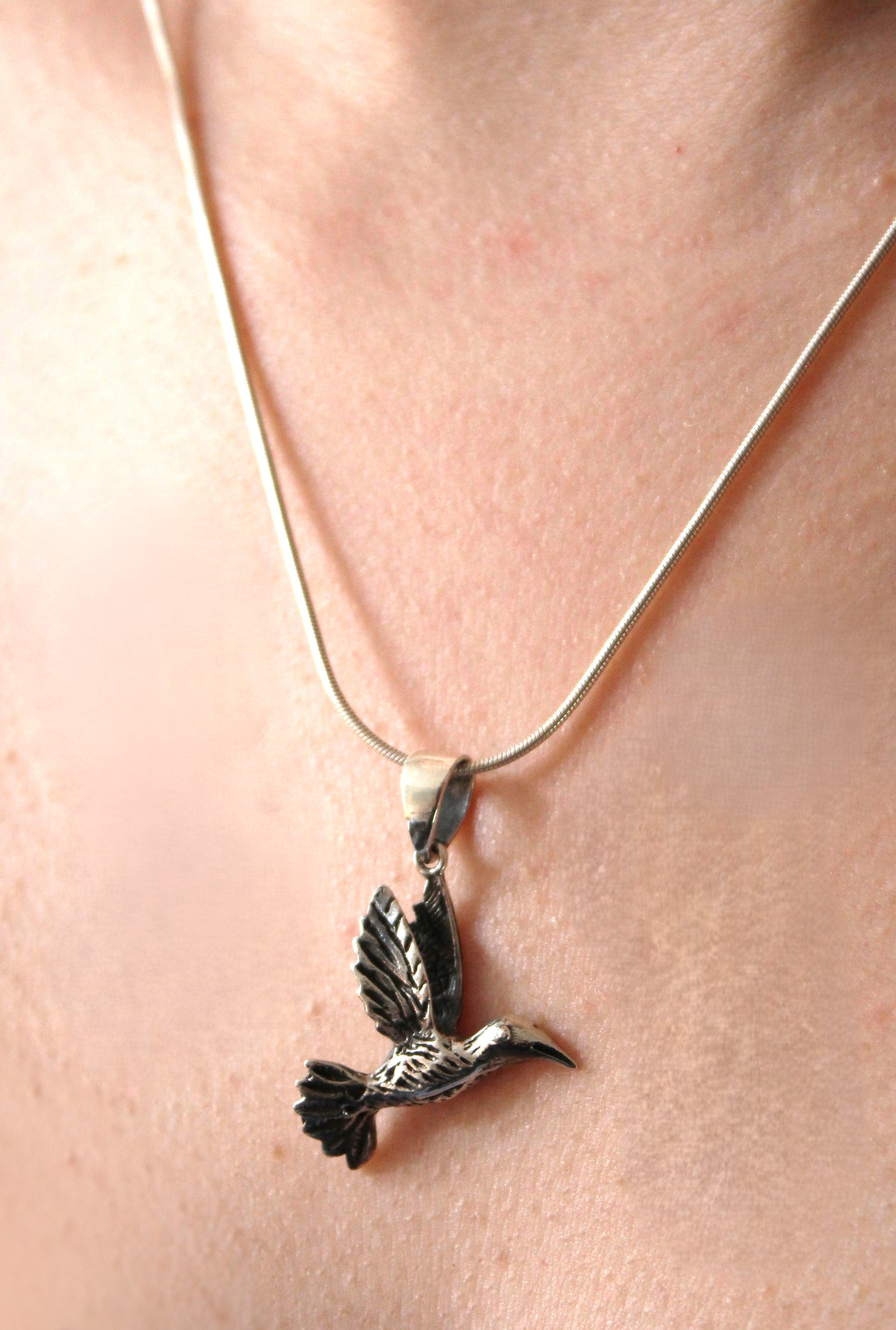 A close-up of the Watermelon Tropical Wildlife Pendant - Bird In Flight With Chain, featuring a detailed bird design resting on bare skin—ideal for fans of nature-inspired jewelry.