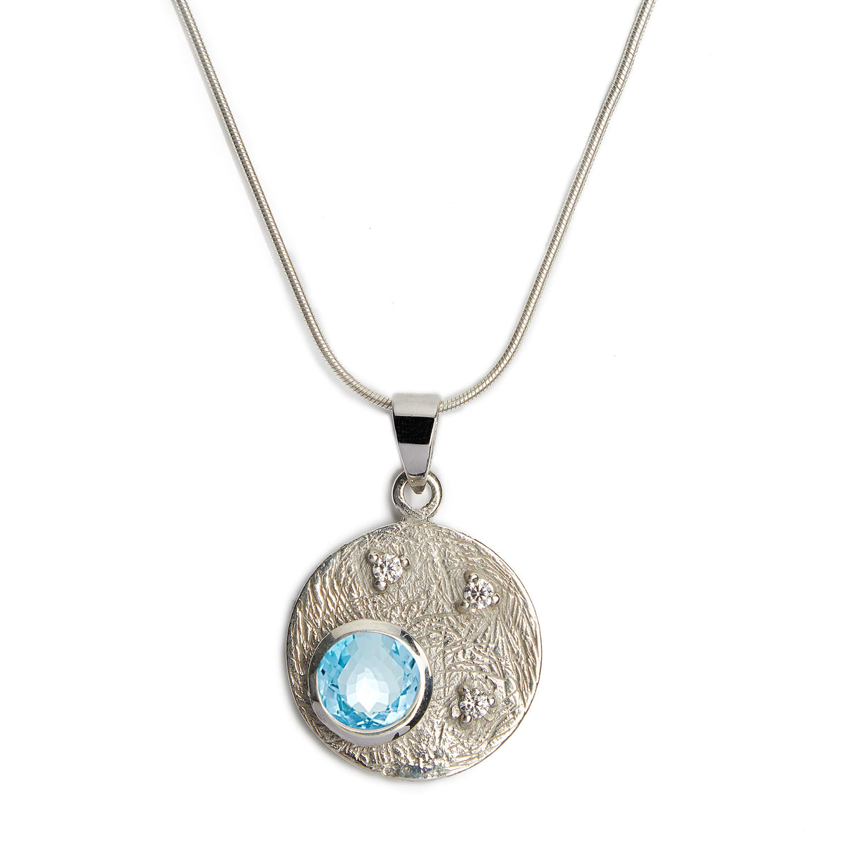 Introducing the Celeste Necklace in Silver & various gemstones by Gallardo & Blaine Designs, a sterling silver piece featuring a round pendant. The pendant showcases a textured design with small embedded crystals and a larger central blue cubic zirconia g