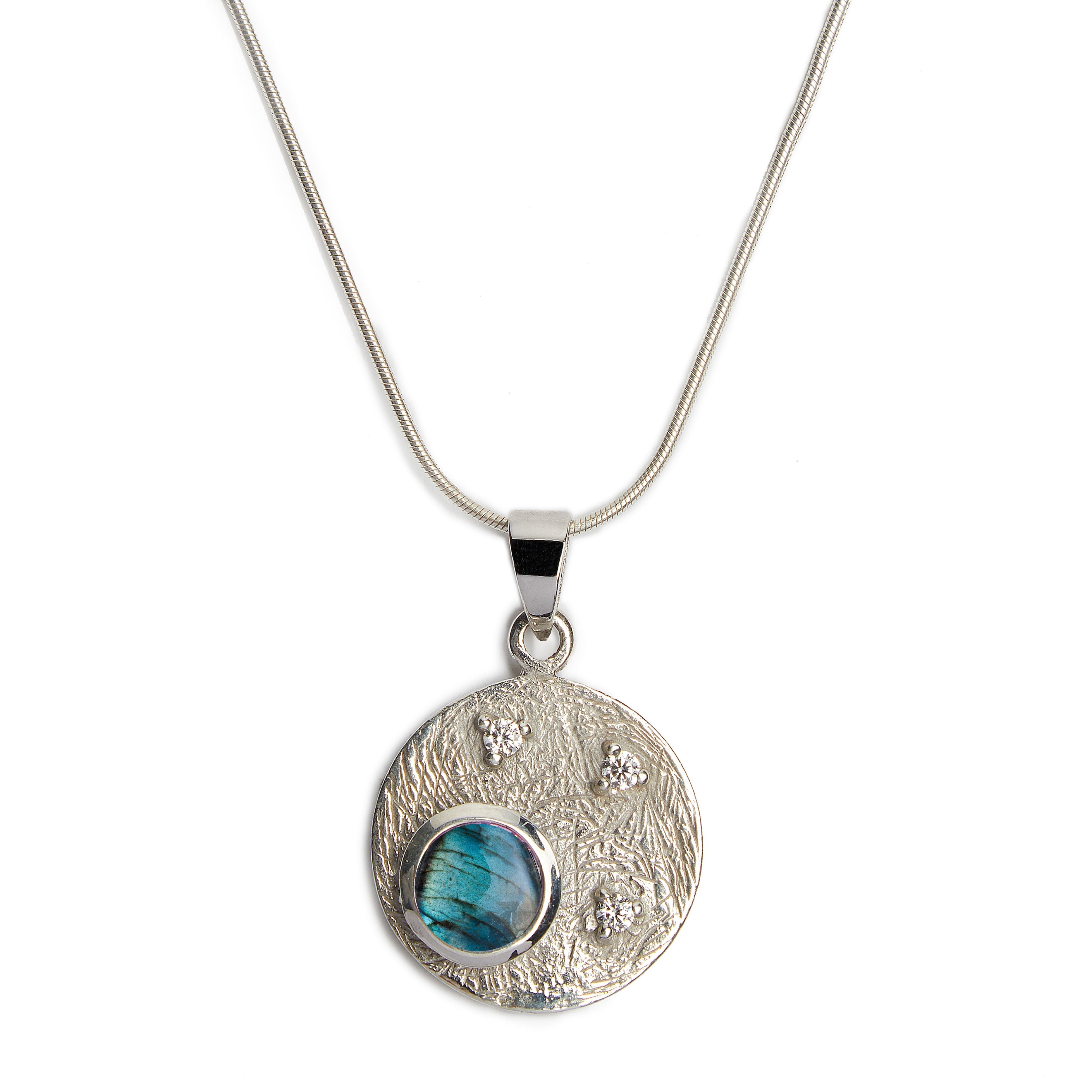 Introducing the Celeste Necklace in Silver & various gemstones by Gallardo & Blaine Designs: A sterling silver piece featuring a round pendant with a textured surface. The pendant showcases three small, cubic zirconia stones and a larger, iridescent blue-