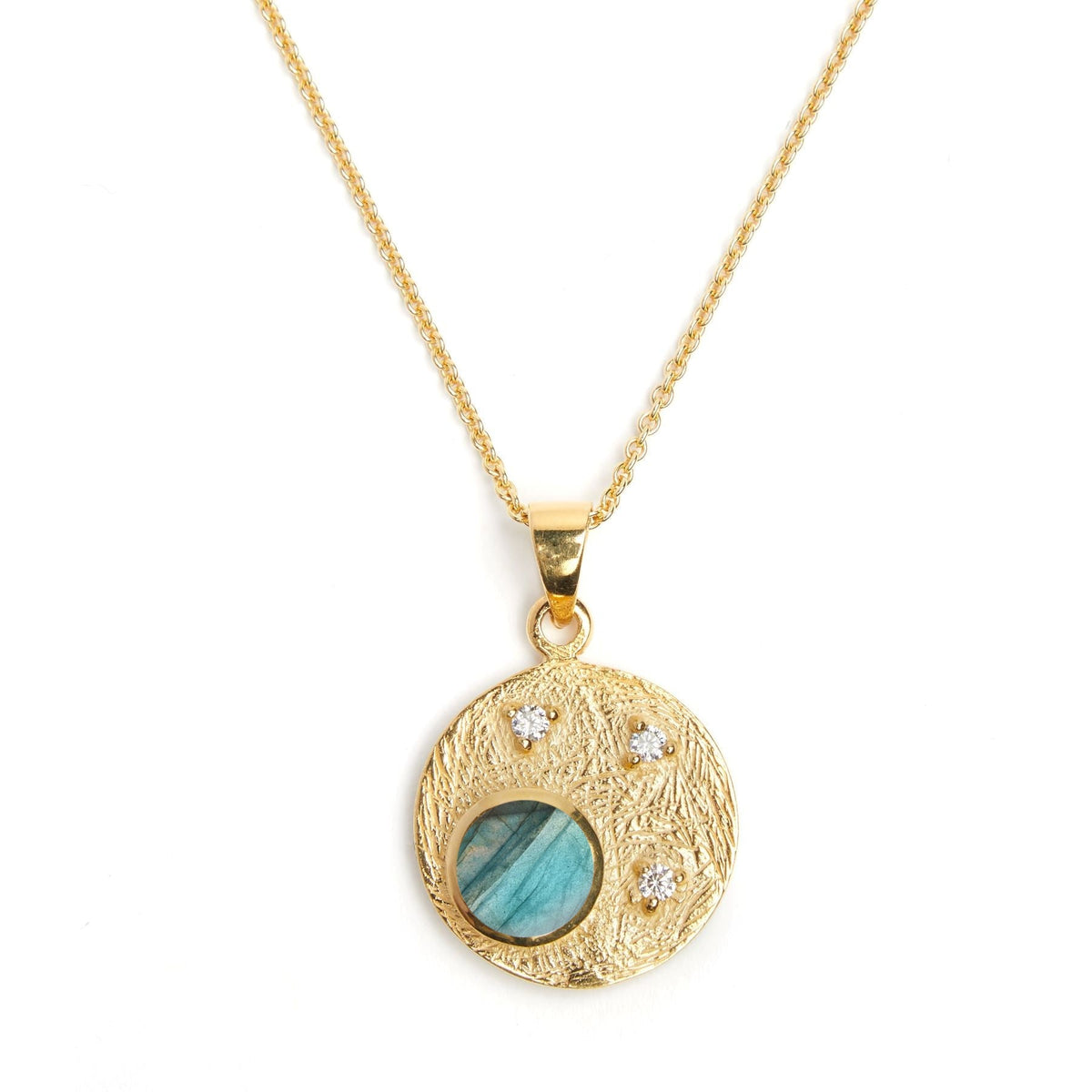 A Gallardo & Blaine Designs Celeste Necklace in Gold & various gemstones with a textured circular pendant featuring a blue-green gemstone in the center, accented by three small white cubic zirconia stones arranged in a triangular pattern. The stunning gem