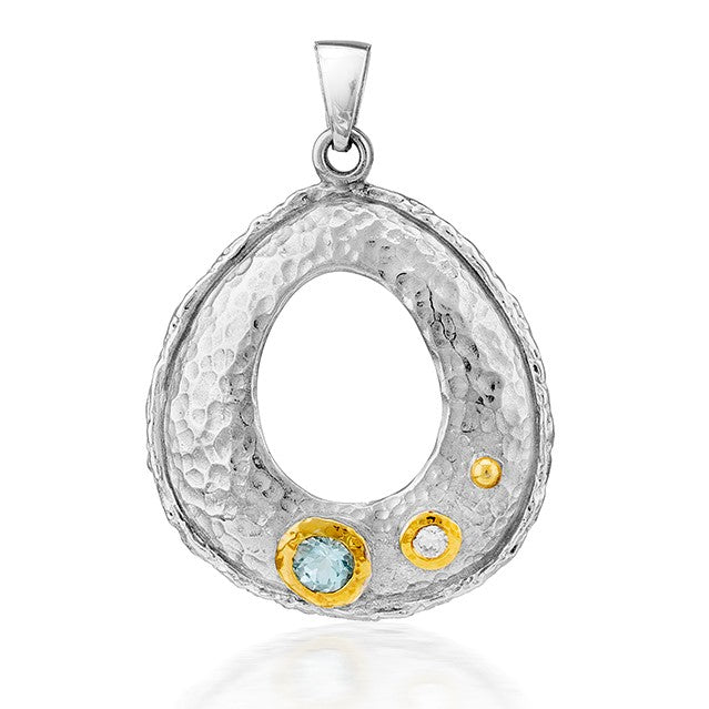 The Ceres Pendant by Gallardo & Blaine Designs features a hammered sterling silver oval with a large blue gem and two small white stones in yellow-gold bezels, offering a striking gemstone look.