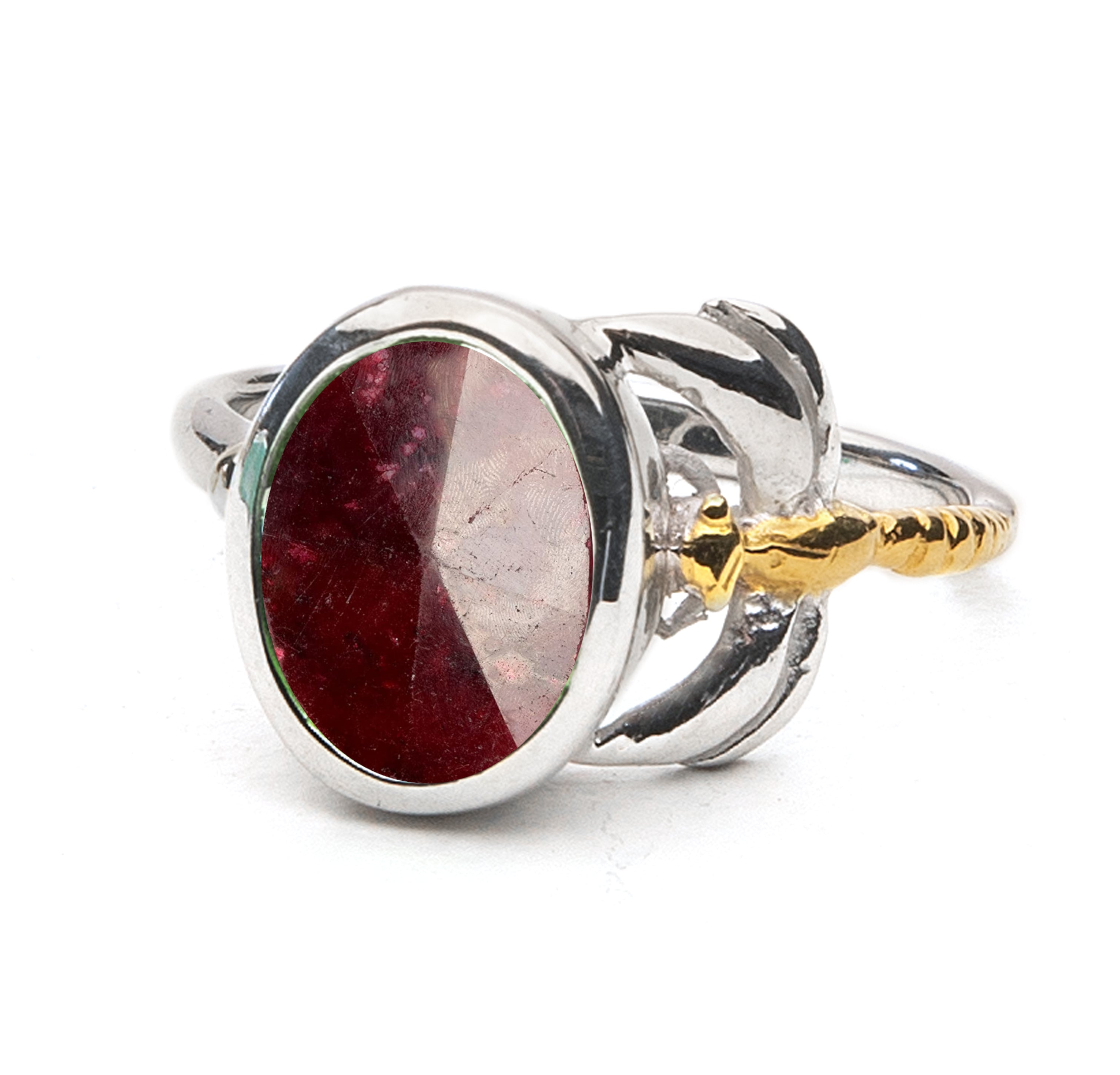 A silver ring featuring a large, oval-shaped red gemstone set in the center. The band has intricate detailing with a mix of silver and gold tones, creating a unique, elegant design. This timeless piece boasts a faceted surface that catches the light beaut