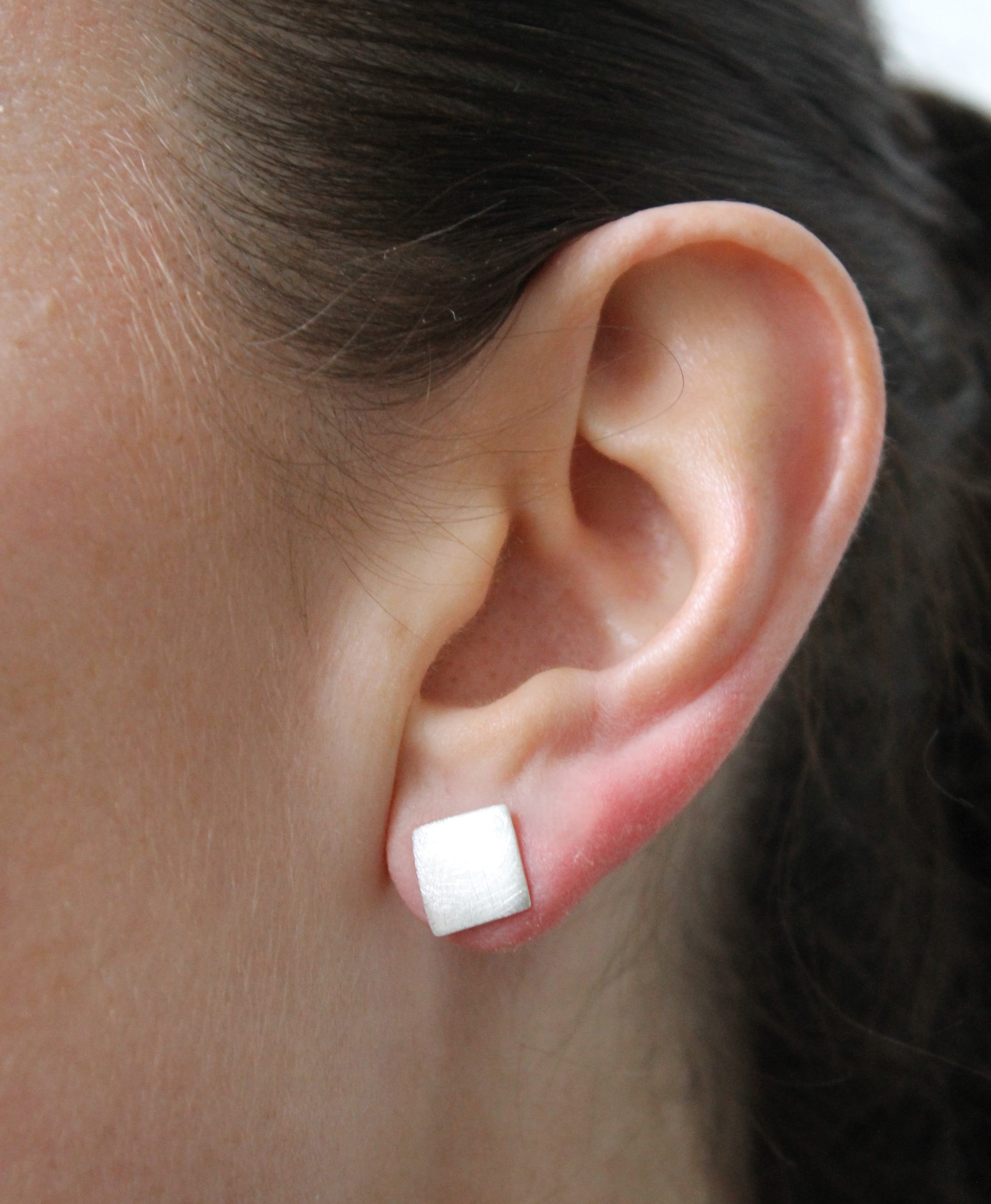 Close-up of a person's ear wearing Gallardo & Blaine Designs' Deco Square Studs in silver, with the elegant, small square shape highlighted against an out-of-focus background.
