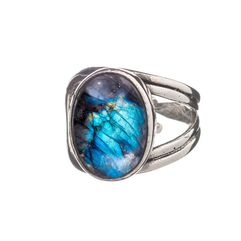 A Gallardo & Blaine Designs Dewberry Ring in various gemstones, featuring an oval-shaped, polished labradorite stone. The stone showcases vibrant shades of blue, green, and a bit of metallic sheen. The adjustable ring band has a split design, adding an el