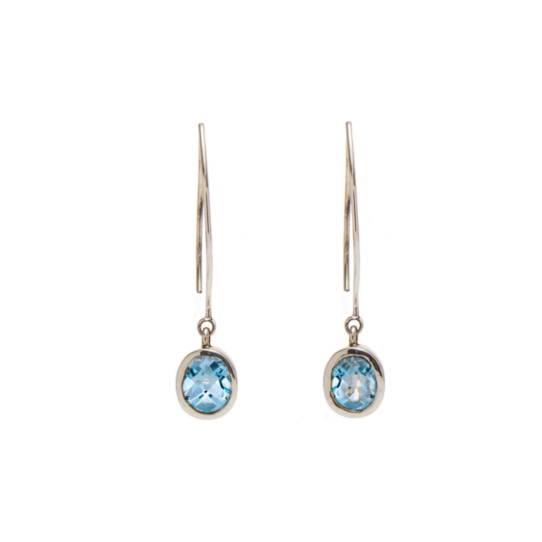 A pair of elegant Dew Drop Earrings in various gemstones featuring oval-shaped blue gemstones by Gallardo & Blaine Designs. The stones are set in a simple, silver-toned bezel setting, hanging from sleek, curved hooks. The minimalistic design highlights th