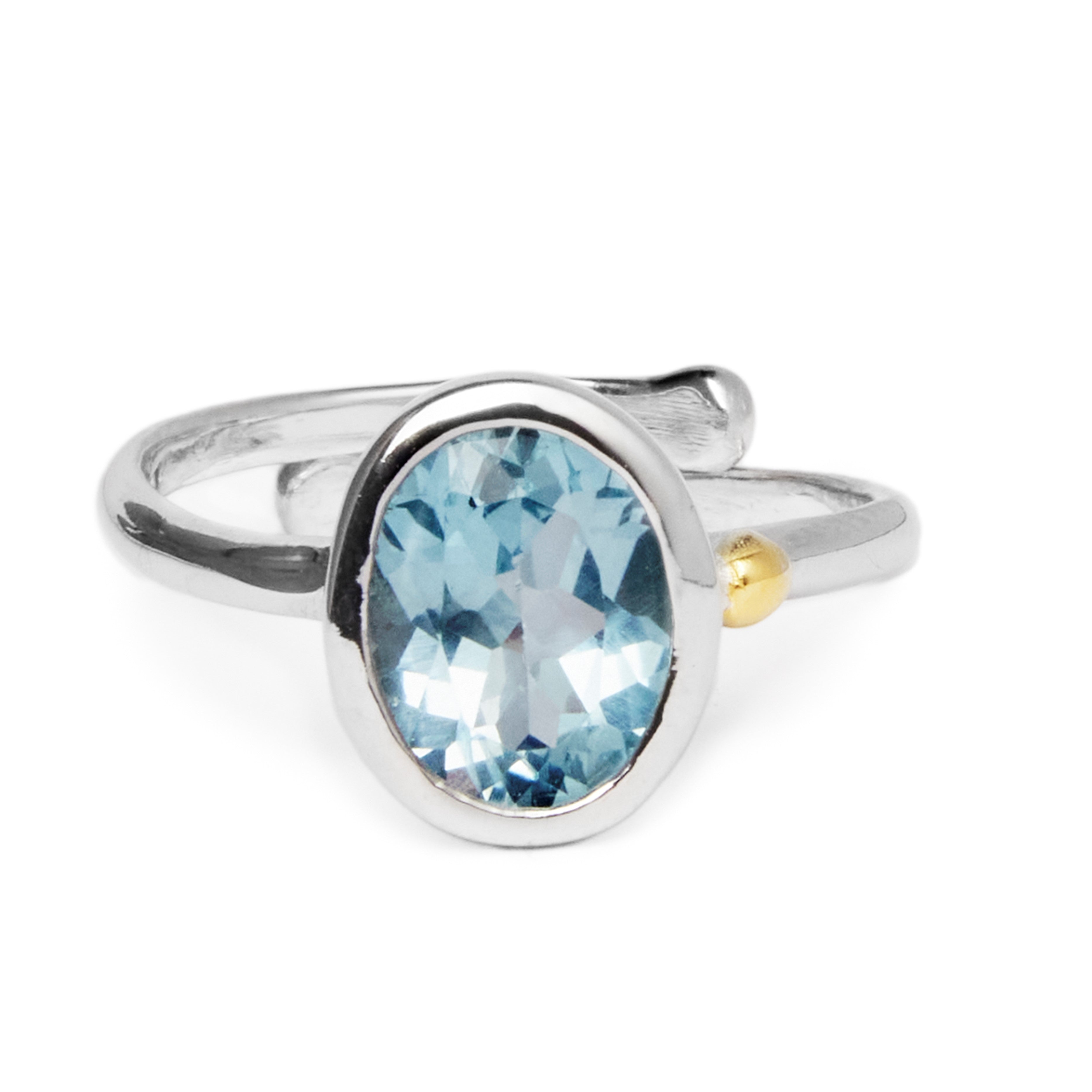 The Gallardo & Blaine Designs Dream Ring in various gemstones features an oval-shaped blue gemstone as its centerpiece. The band of the ring is sleek and polished, showcasing minimalist design with a small gold accent on one side near the faceted stone, r