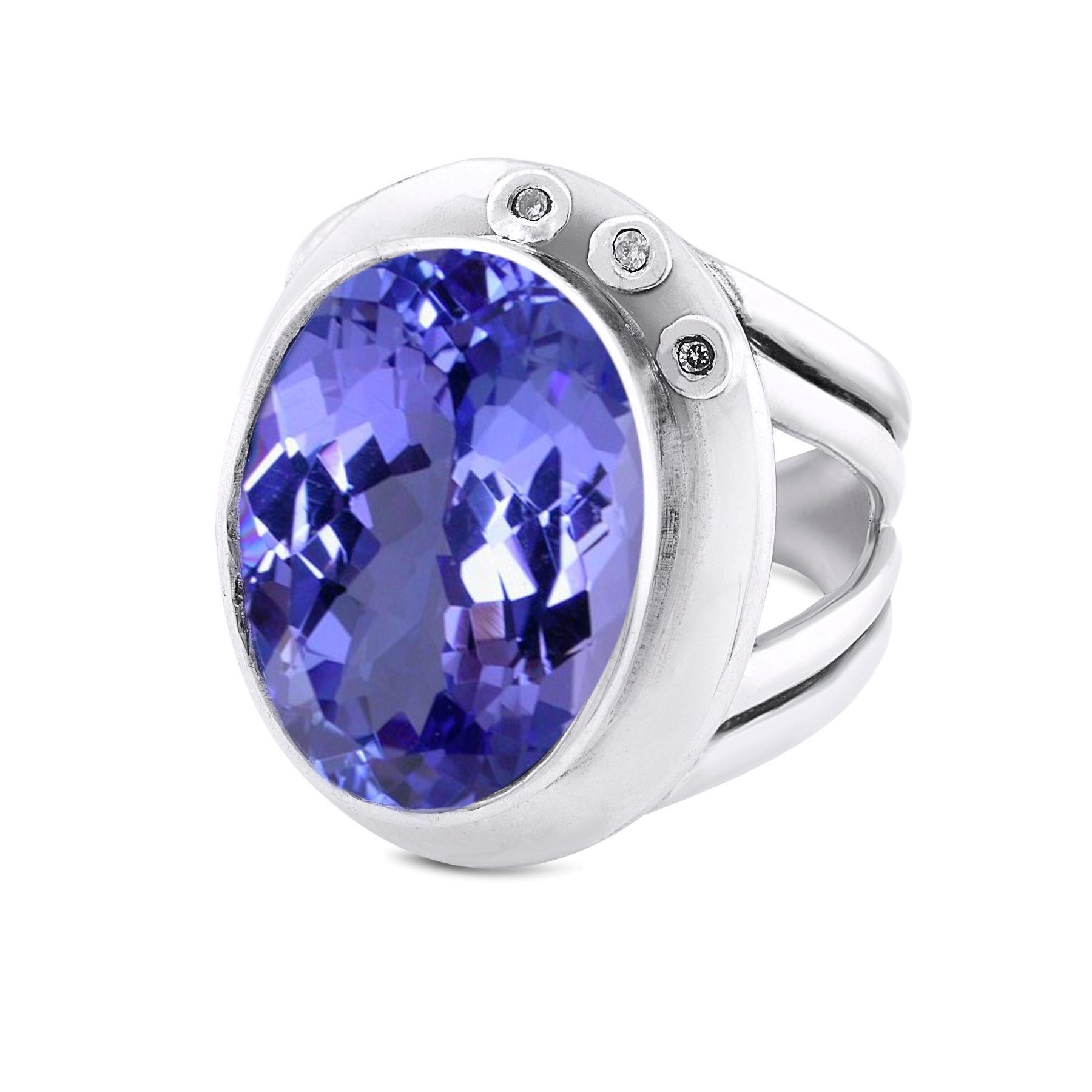 A silver statement cocktail ring featuring a large, oval-shaped purple gemstone set in the center. The band has a unique, open design with two thin strips on each side. Additionally, this ring is adorned with three small round diamonds on the side of the