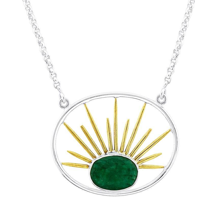 A silver Goddess Necklace Large in Various Gemstones with a gold vermeil chain features a circular pendant. Inside the circle, a green gemstone is set at the bottom center, with golden sunray-like lines radiating outward and upward from it, creating a sun