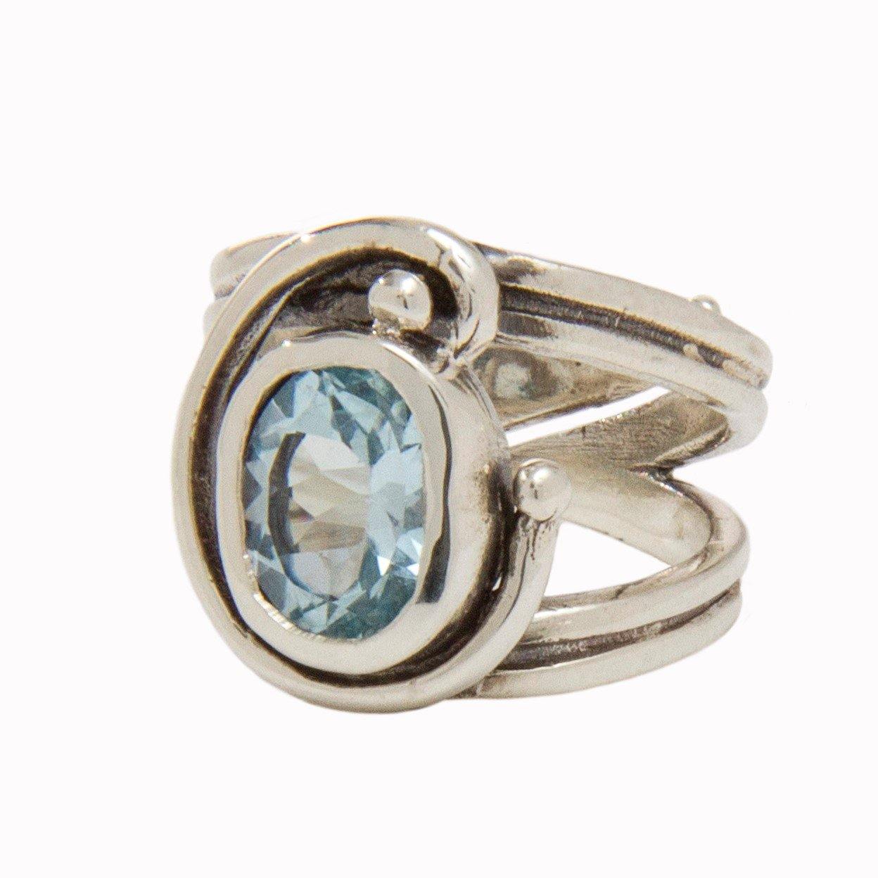 The Jasmine Ring by Gallardo & Blaine Designs features an open, swirling Art Nouveau silver band with an oval-cut light blue gemstone at the center, offering an elegant and adjustable fit.