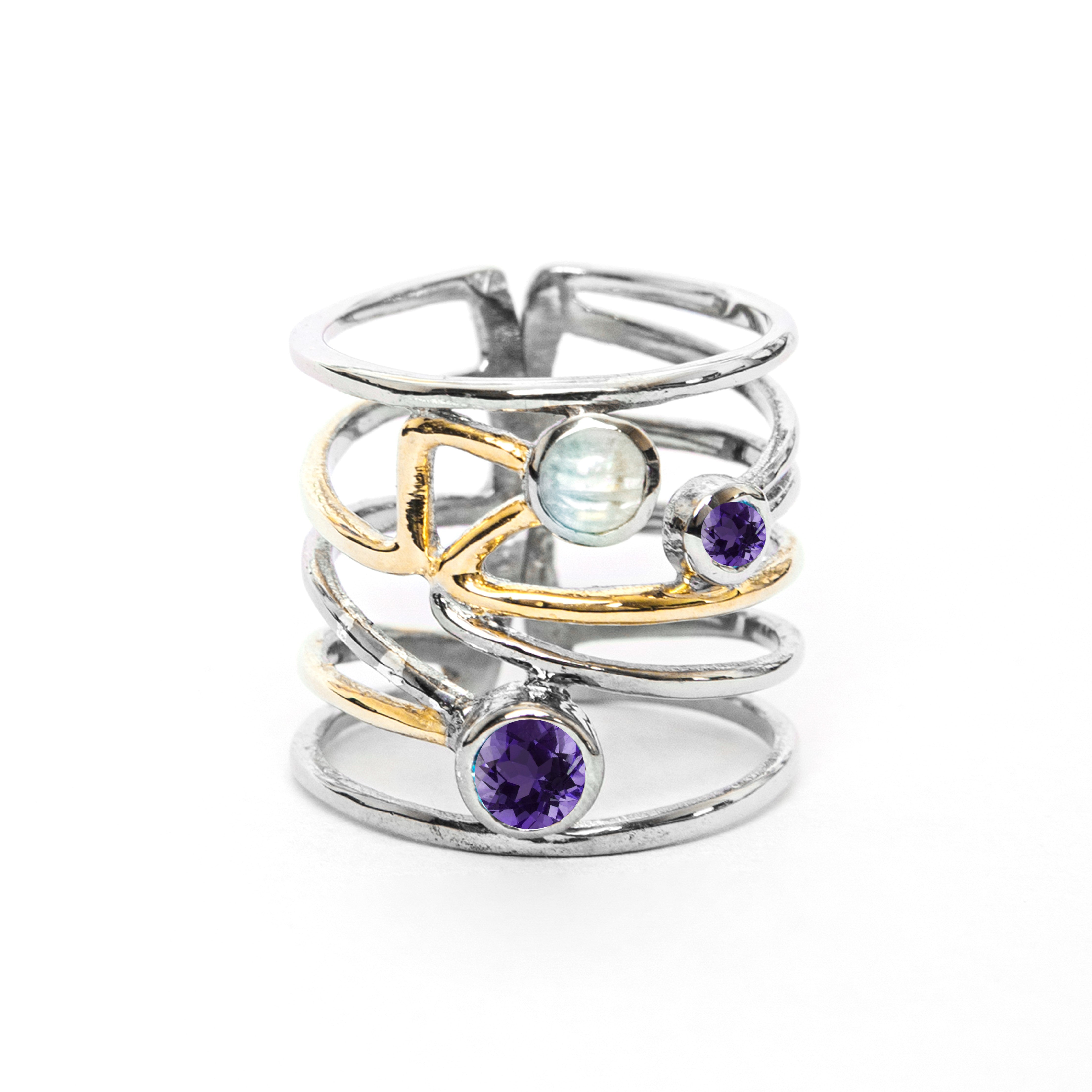 A stylish silver Lattice Ring in various gemstones by Gallardo & Blaine Designs featuring a contemporary, open band design with crisscrossing golden and silver bands. It is adorned with a blue moonstone and two purple gemstones, adding an elegant touch to