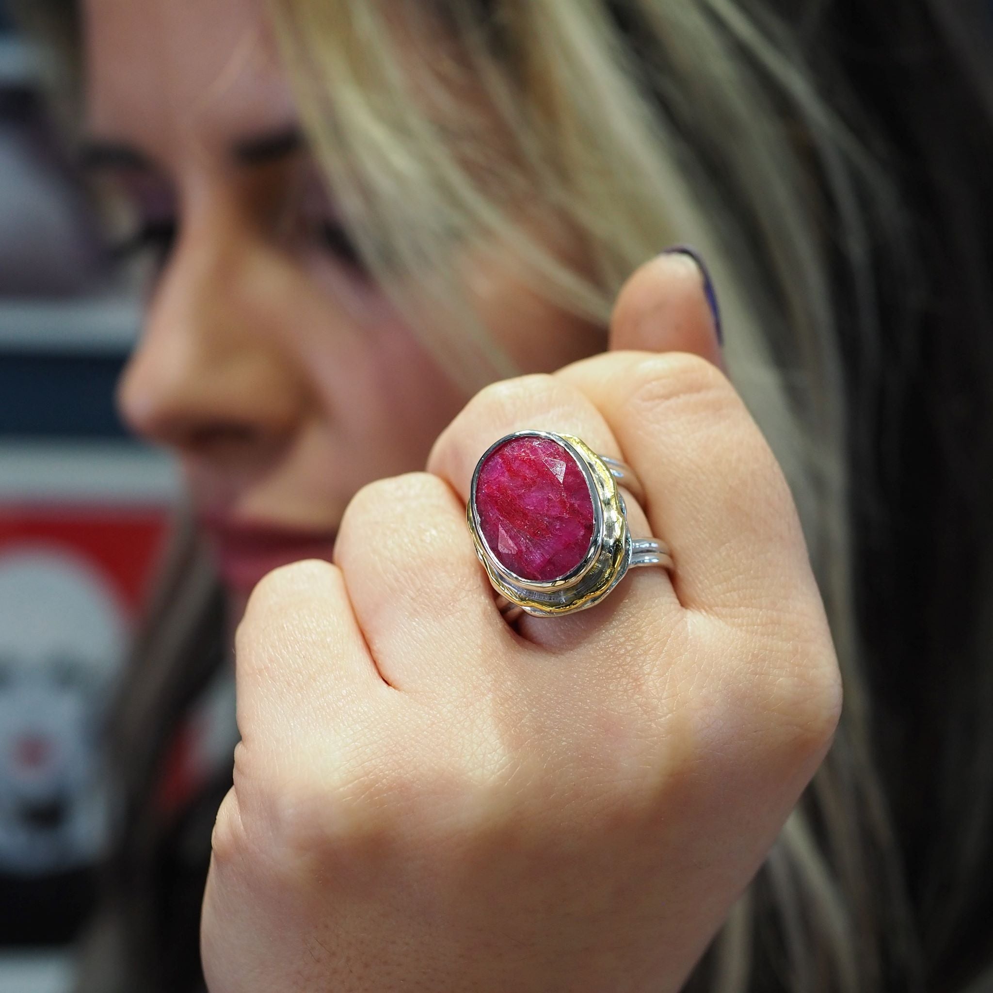 Close-up of a person holding up a hand to display a large, oval red gemstone set in a silver band with a gold accent. The Magnolia Ring in silver gold & various gemstones by Gallardo & Blaine Designs stands out as an exquisite statement ring, with the blu