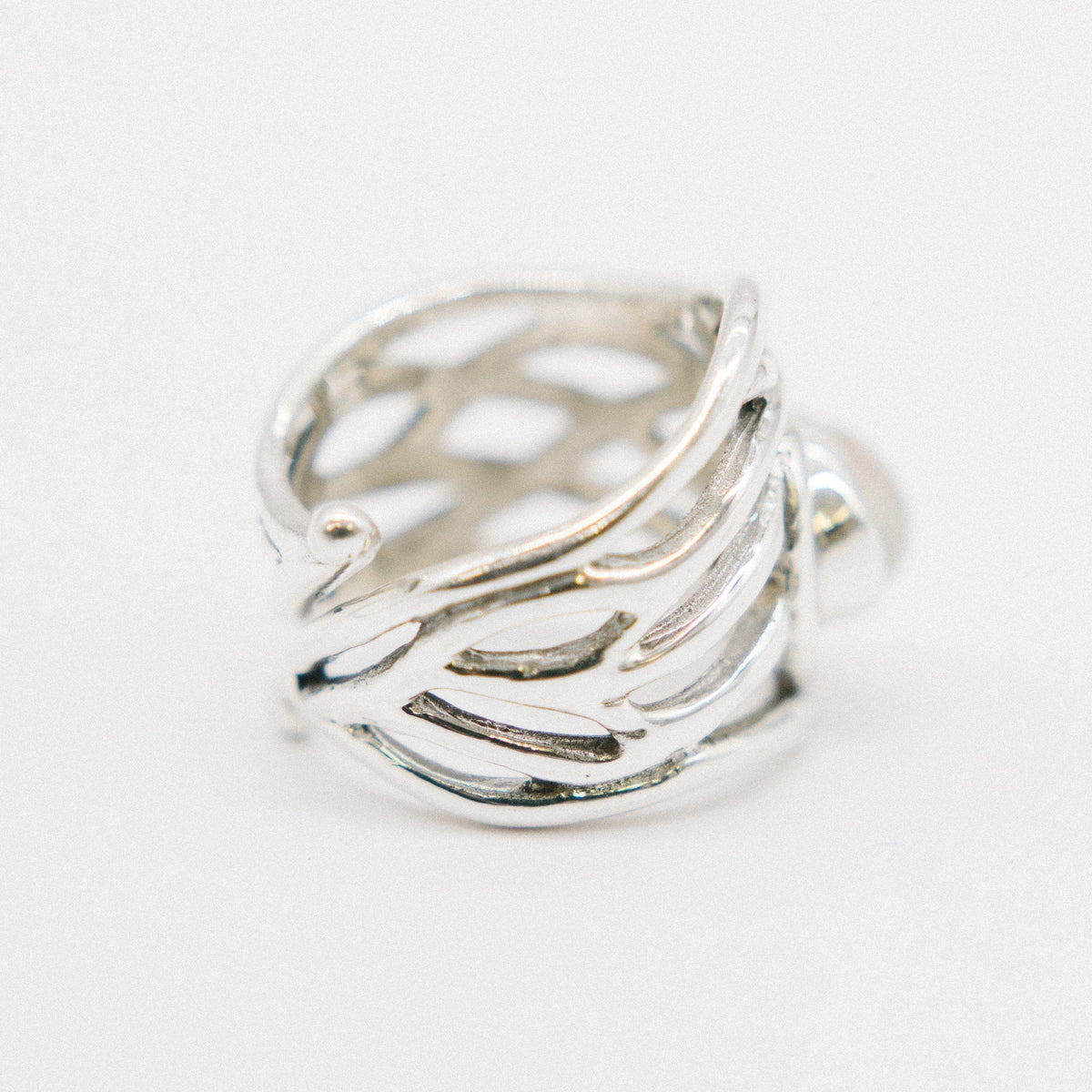 A close-up image of a chunky statement ring with an intricate, openwork design. The band features a pattern resembling interwoven strands, giving it a light and airy appearance. The Mayhem Ring in various gemstones by Gallardo & Blaine Designs is position