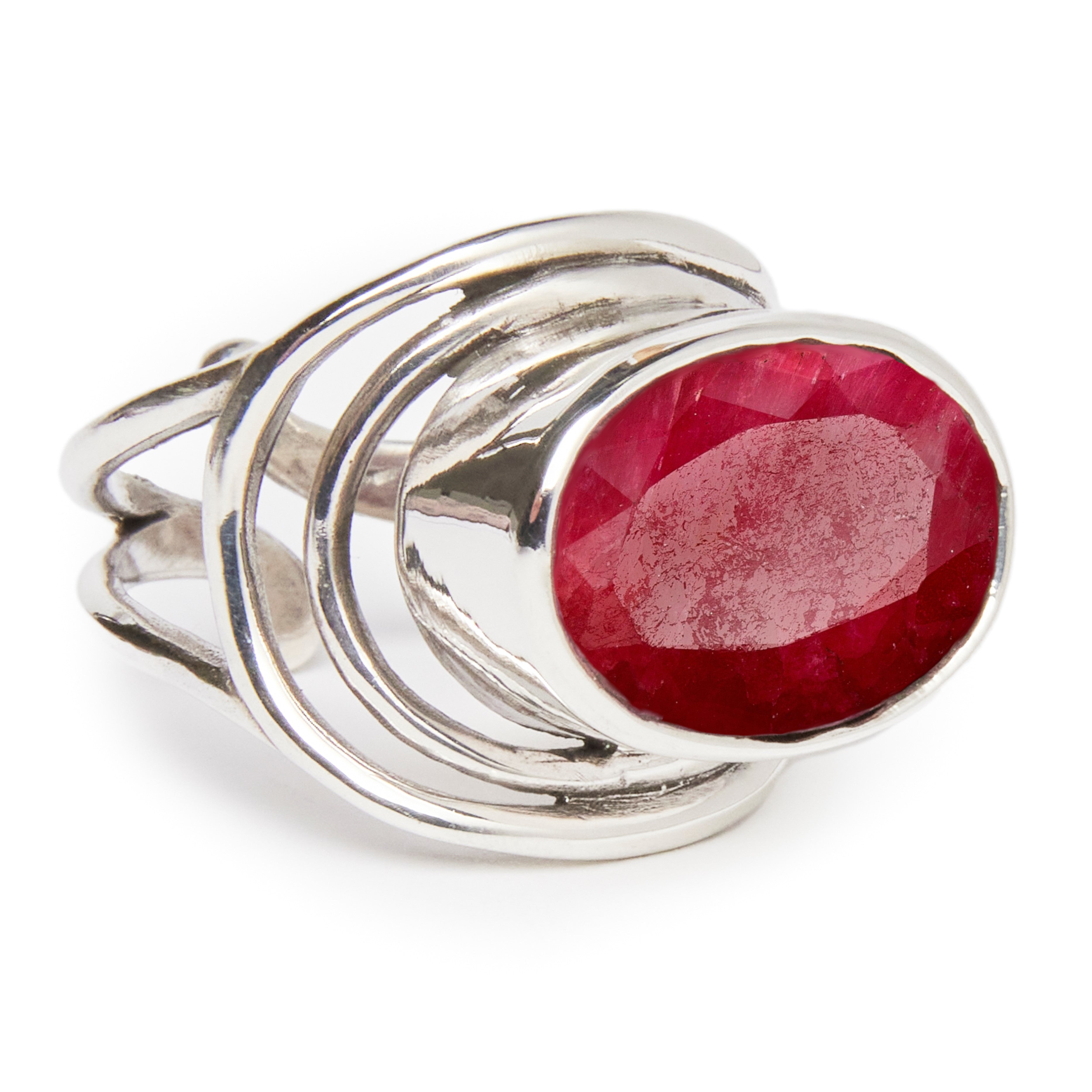 The Party Ring by Gallardo & Blaine Designs is a chunky silver statement piece with an oval-cut red gemstone. Its intricate swirling band loops around the faceted gem, reflecting light beautifully to stand out as a striking accessory.