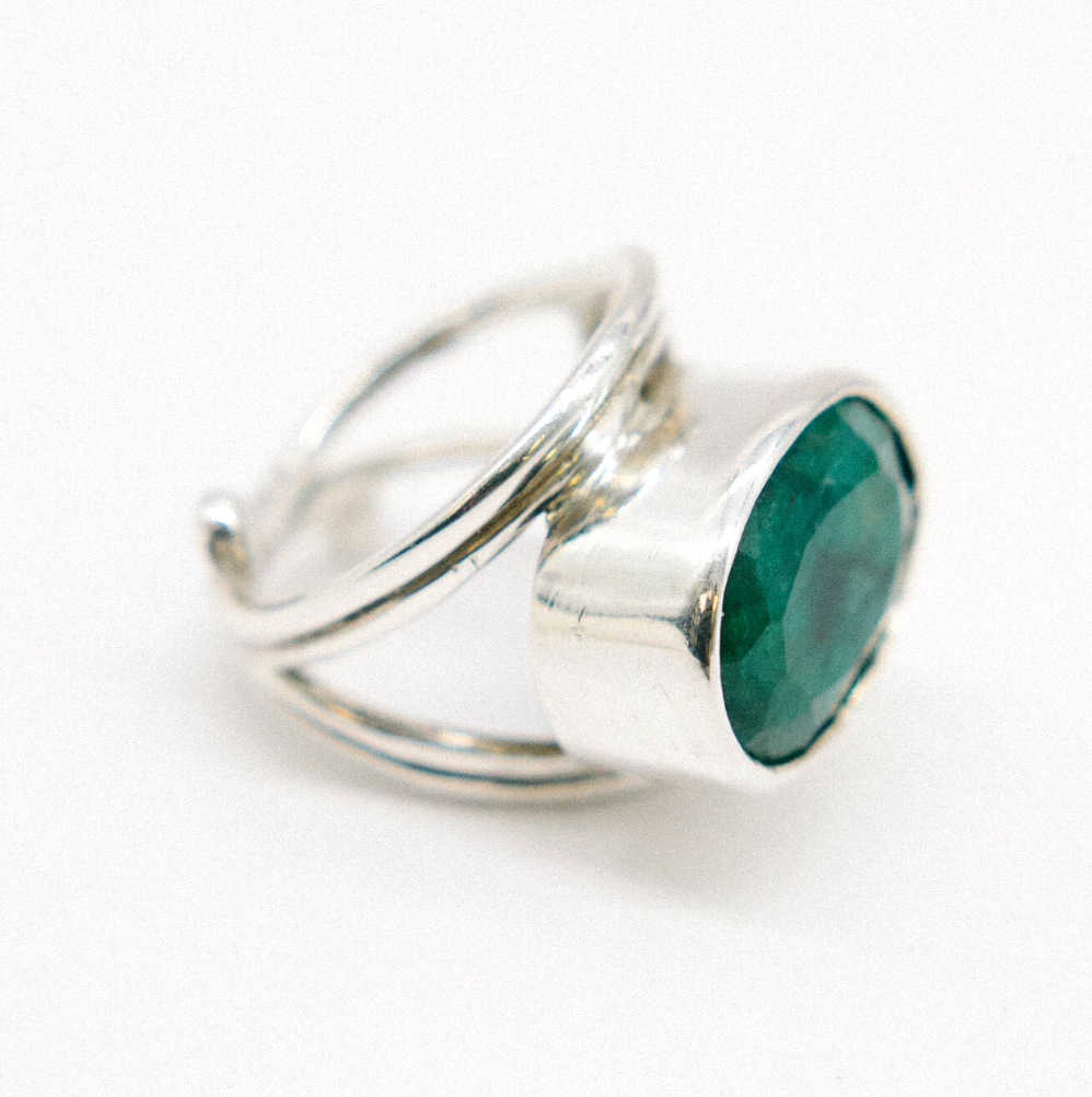The Party Ring by Gallardo & Blaine Designs features a large round green gemstone in a thick bezel, set on an intricately designed band with multiple loops, creating an elegant and artistic flair.