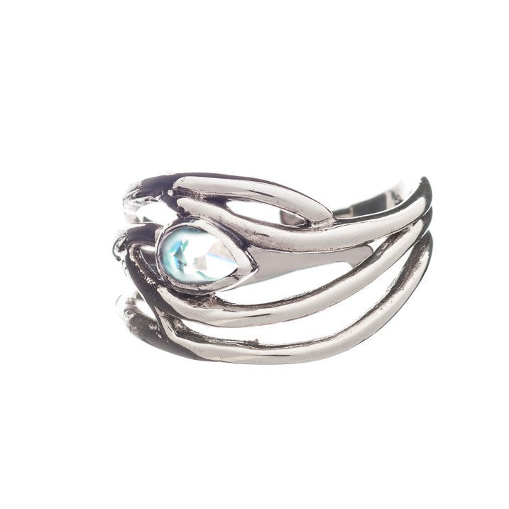A silver Peacock Ring in various gemstones with an intricate, sculptural design features a central, teardrop-shaped light blue gemstone. The metalwork has a flowing, organic aesthetic, clasping the gemstone securely. This elegant dainty ring by Gallardo &