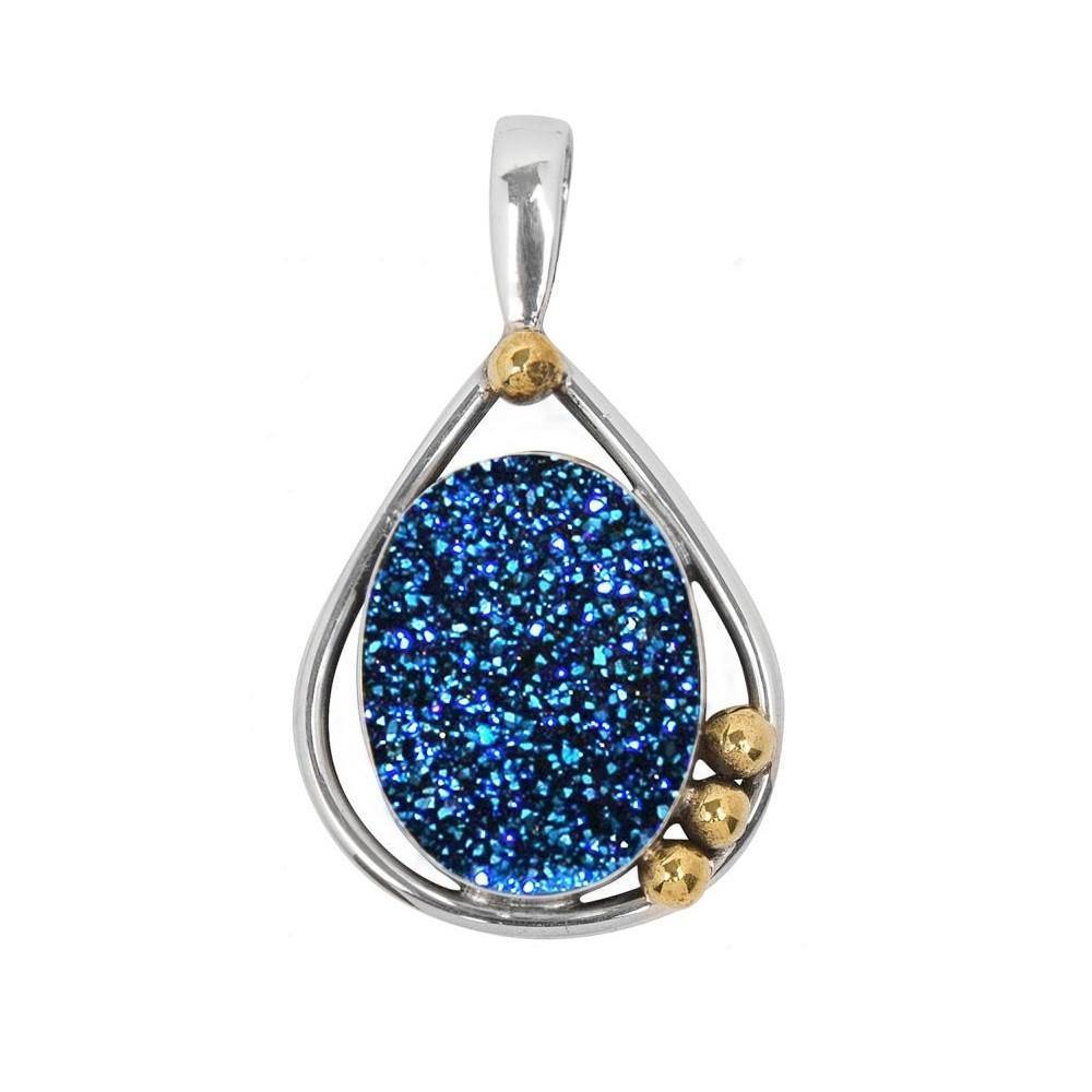 The Poppy Pendant Medium In Blue Druzy by Gallardo & Blaine Designs showcases a teardrop-shaped sterling silver frame featuring a glittery blue druzy stone at the center. The design includes three small gold spheres on the right side of the frame, adding