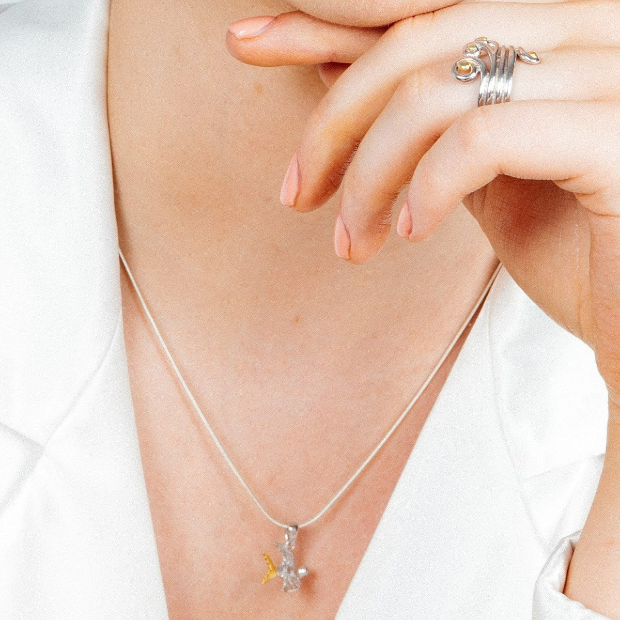 Close-up of a person wearing a sterling silver snake chain necklace with a small Wildlife Pendant - Swallow With Chain by Gallardo & Blaine Designs and a silver ring featuring an orange stone on their index finger. The person is touching their lips with t