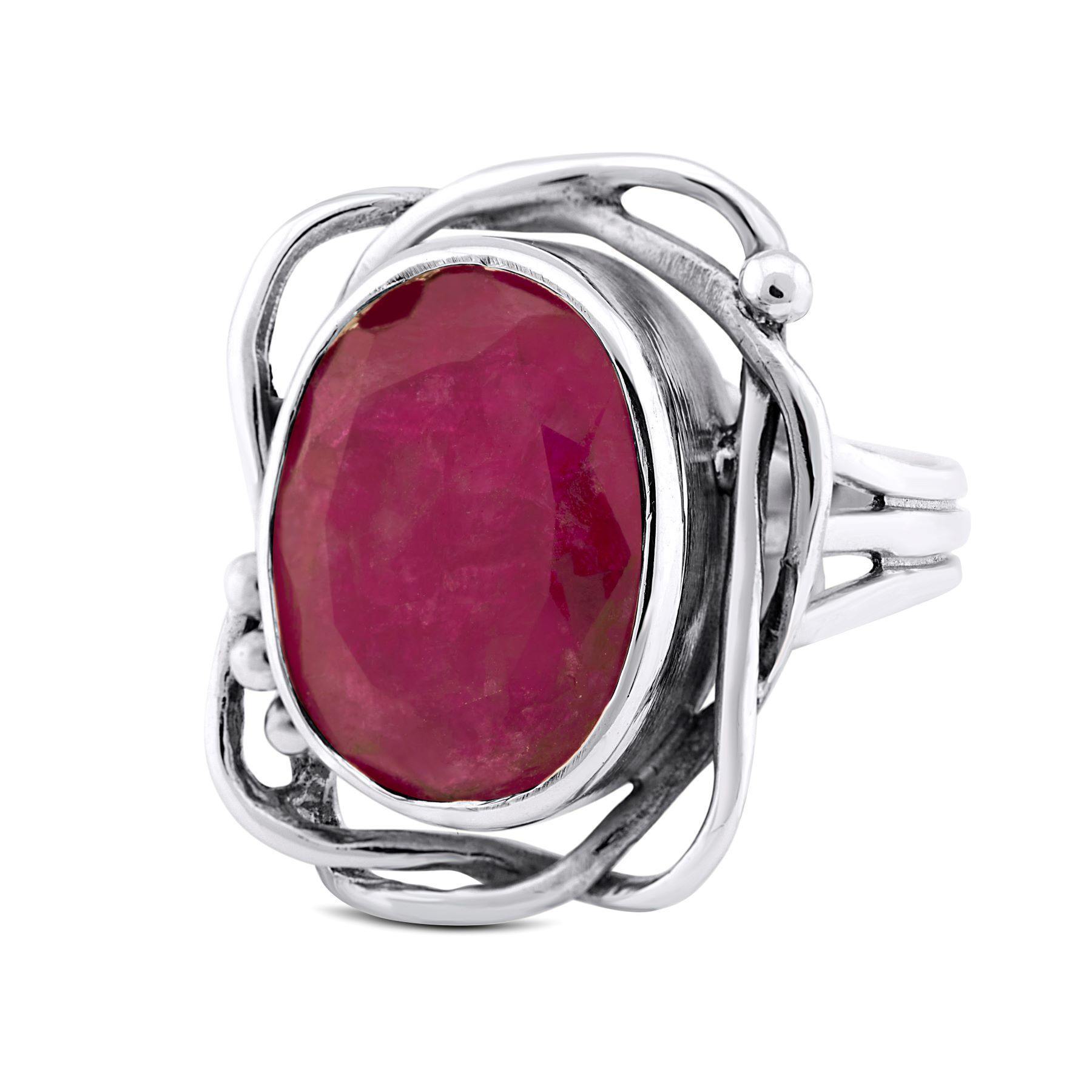 This Gallardo & Blaine Designs Whirlpool Ring in various gemstones features an oval-shaped, faceted ruby gemstone in the center. The ruby is encased in an intricate, openwork silver setting with swirling patterns, creating an elegant and artistic design.