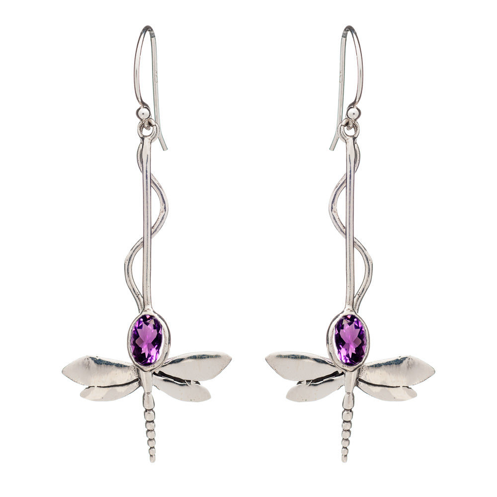 A pair of Willow Earrings in Various Gemstones by Gallardo & Blaine Designs with elongated hooks. The dragonflies boast detailed wings and bodies, featuring oval-shaped purple gemstones set in their centers. The twisted pattern of the hooks elegantly lead