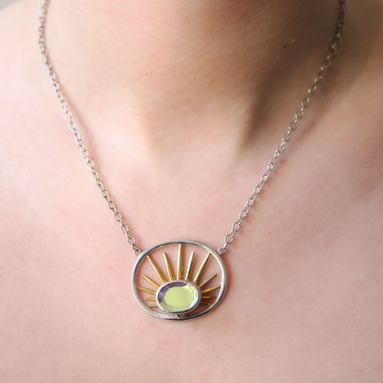 The Goddess Necklace Small by Gallardo & Blaine Designs features a circular pendant with a yellow-green gemstone and gold rays, elegantly crafted in sterling silver—an exquisite accessory for any neckline.