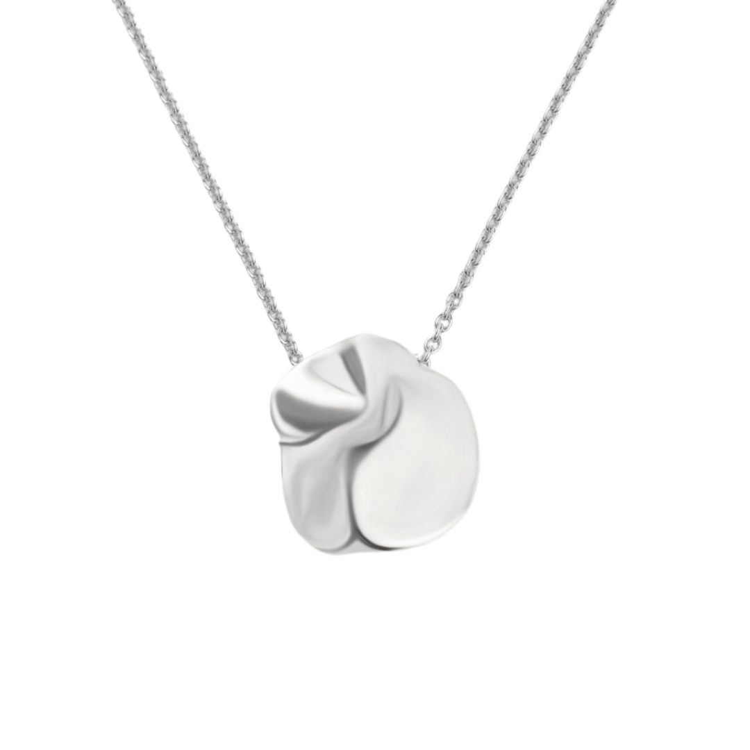 The Madeleine Blaine Tide Necklace features a sculpted, abstract silver pendant with smooth, folded surfaces, hand-carved in Dublin and displayed on a delicate chain against a white background.