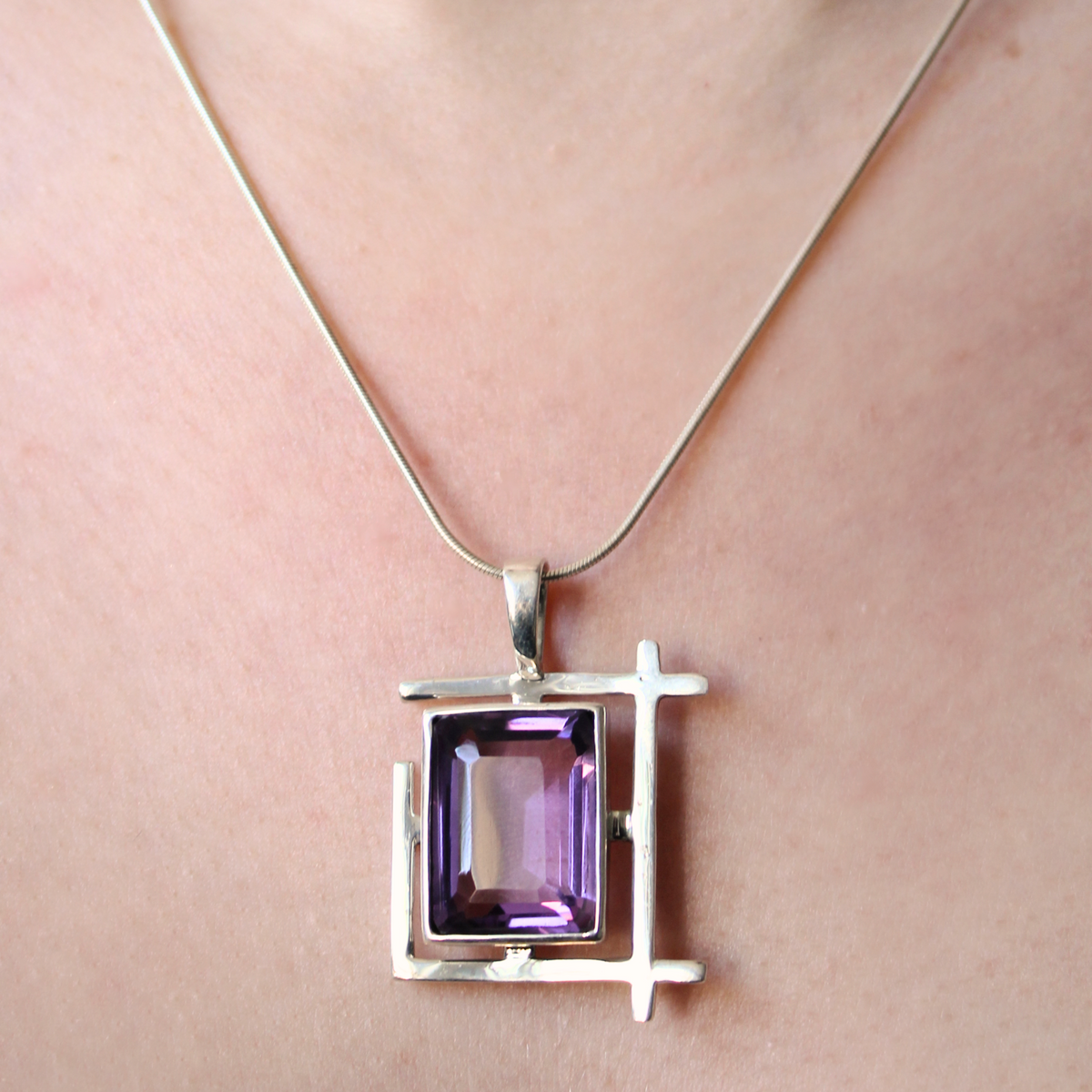 A close-up of the Gallardo & Blaine Designs Art Deco Pendant, featuring a modern geometric design and a square purple gemstone, worn as a sterling silver necklace.
