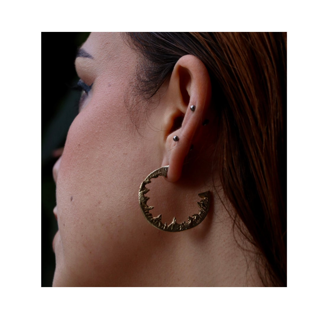 A close-up of an ear with multiple piercings showcases the Elements Hoops by Madeleine Sculptural Jewellery. Brown hair is tucked behind the ear, drawing attention to these unique handmade statement earrings.