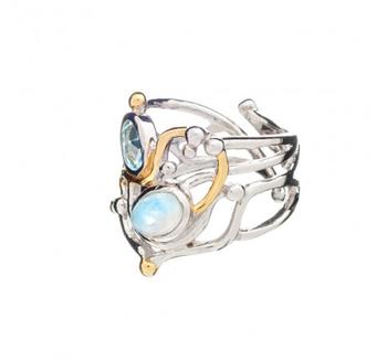 A silver statement ring featuring an intricate, open metalwork design, crafted from sterling silver and adorned with two large gemstones—one blue and one iridescent—as well as small gold vermeil embellishments. This exquisite piece is reminiscent of the o