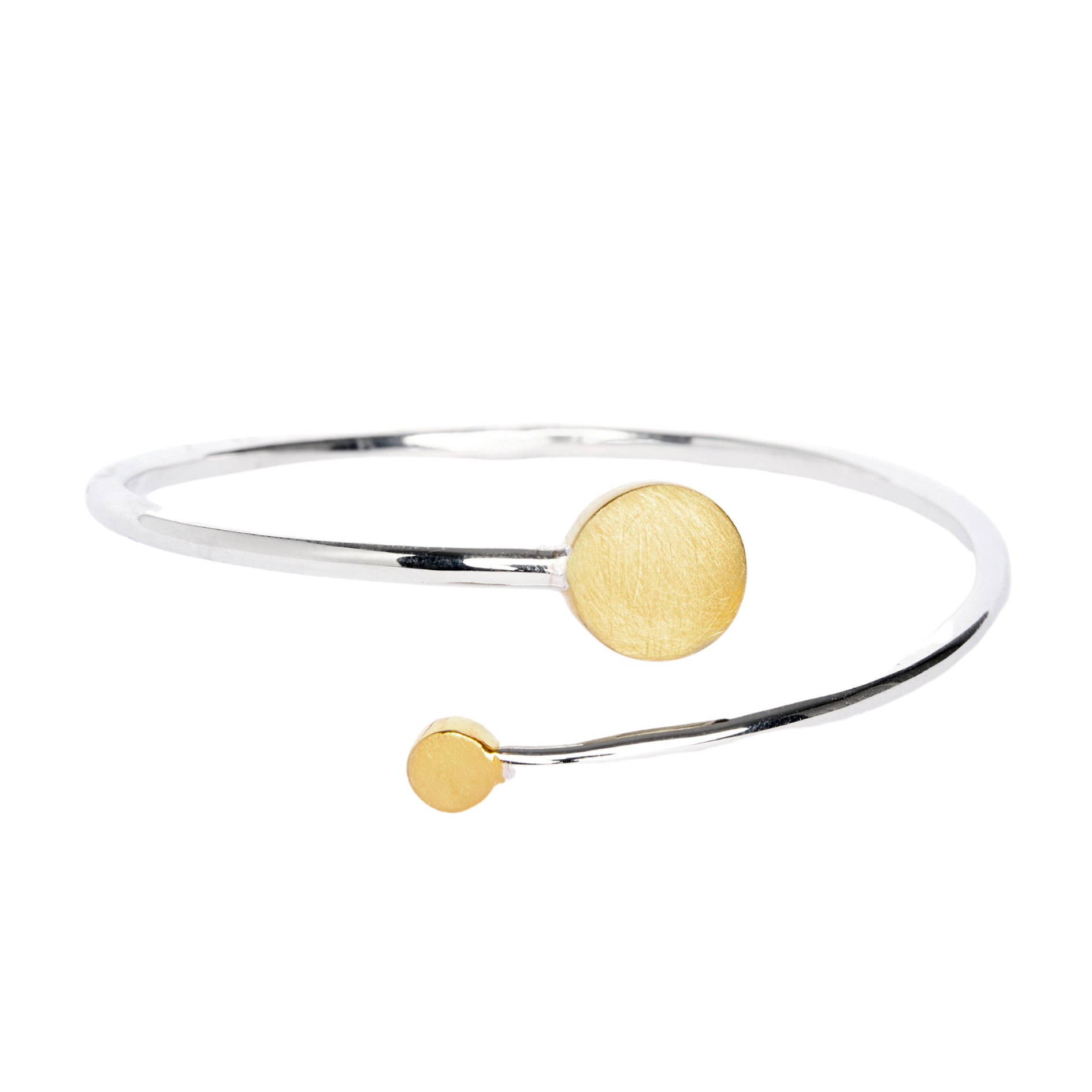The Archeol Bangle by Gallardo & Blaine Designs is a minimalist sterling silver piece with two round, flat gold accents of varying sizes at each end, inspired by classic Irish jewelry and presented on a white background.