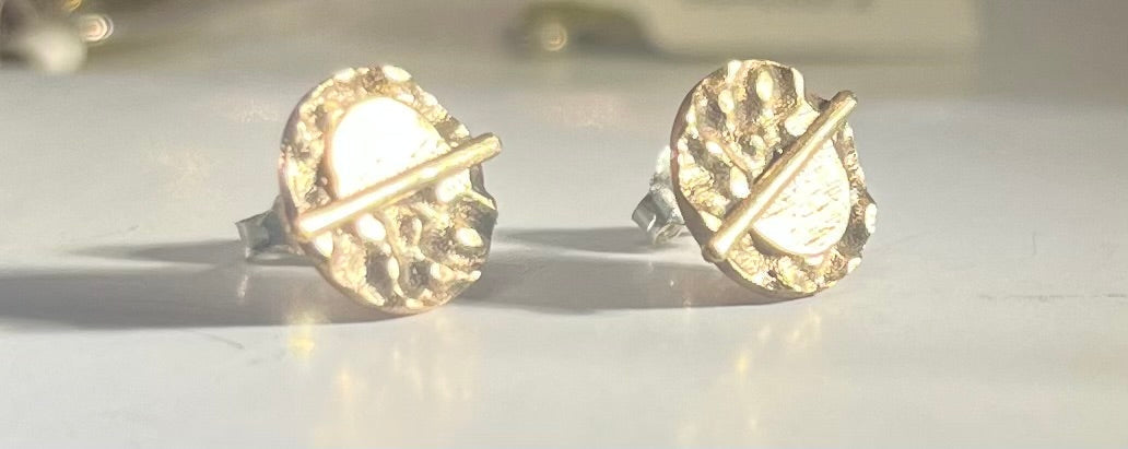 A pair of Lunar Eclipse Stud Earrings by Gallardo & Blaine Designs with circular, textured designs are displayed on a white surface. Each earring features a horizontal bar across its center, adding a unique, modern touch that echoes French elegance. The b