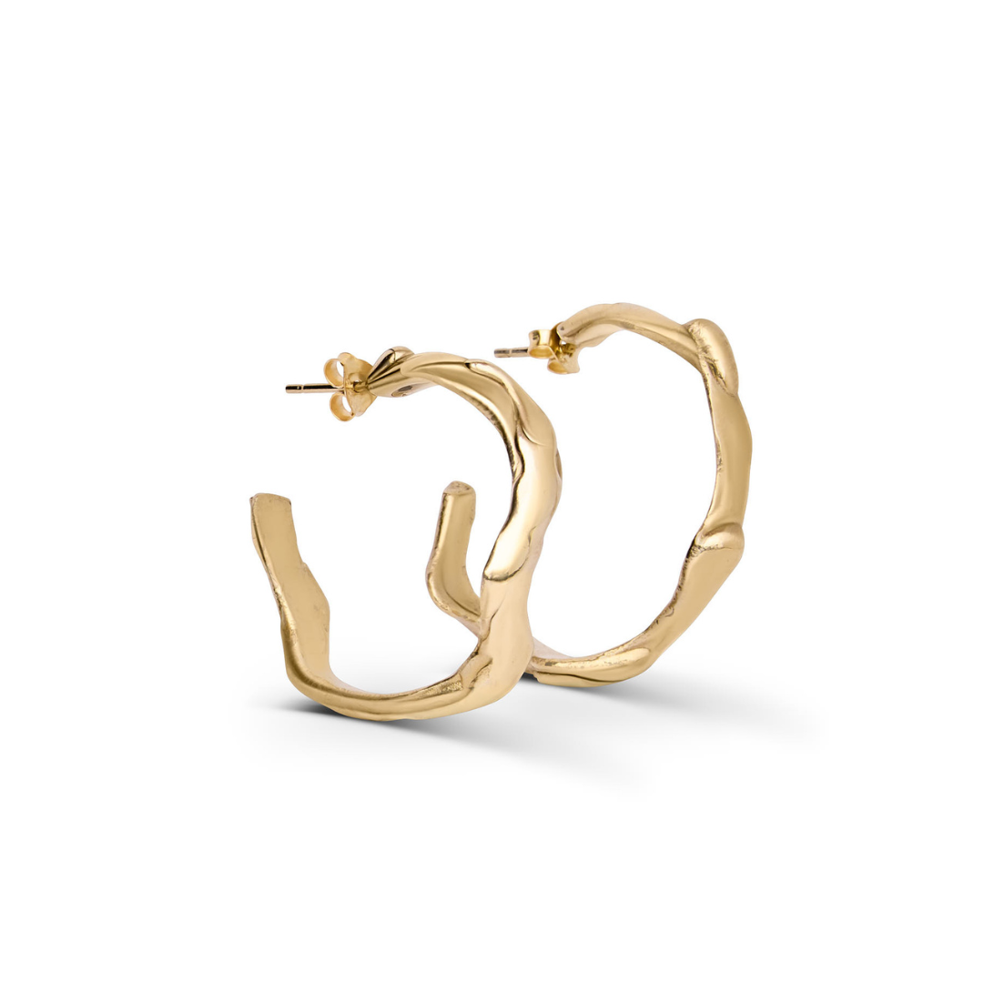 Introducing the Liana Hoops by Madeleine Blaine—gold hoop earrings featuring an organic, wavy design inspired by Dublin’s handcrafted jewelry techniques. These earrings showcase a shiny finish, post back closures, and capture the artistry of hand-carved c