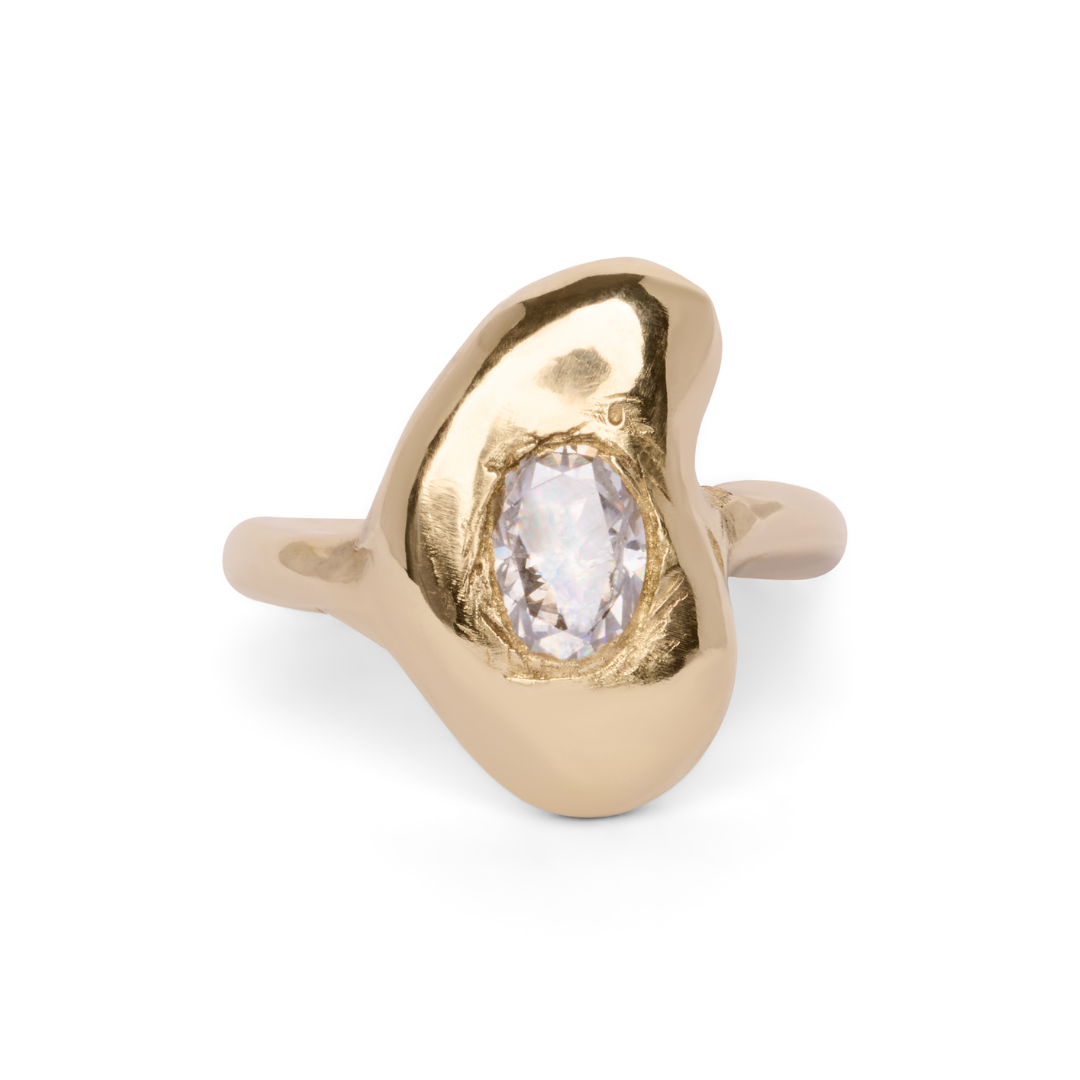 The Carraig Ring by Madeleine Sculptural Jewellery is a one-of-a-kind gold ring with an organic, uneven silhouette, showcasing a central oval-cut clear gemstone set in a polished, abstract bezel.