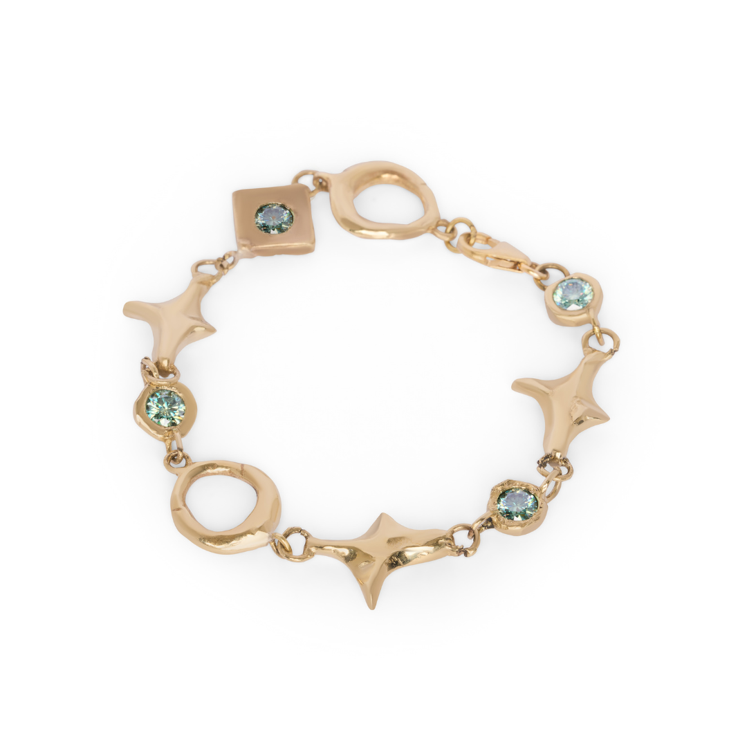 Spark Bracelet in Brass by Madeleine Sculptural Jewellery, featuring geometric shapes—circles, stars, and a square—each adorned with light blue gemstones, displayed on a white background.